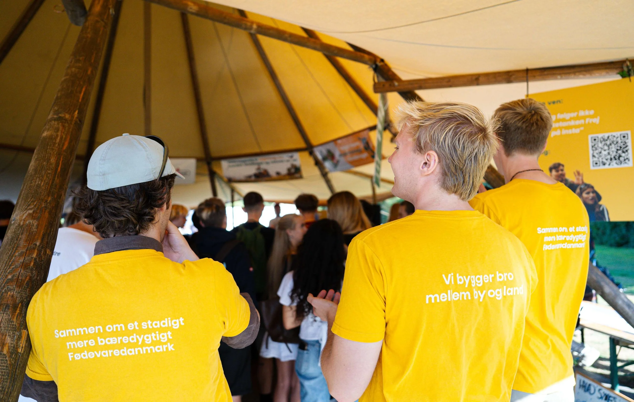 Tre unge mennesker står med ryggen til foran et publikum, de har Tænketanken Frej t-shirts på