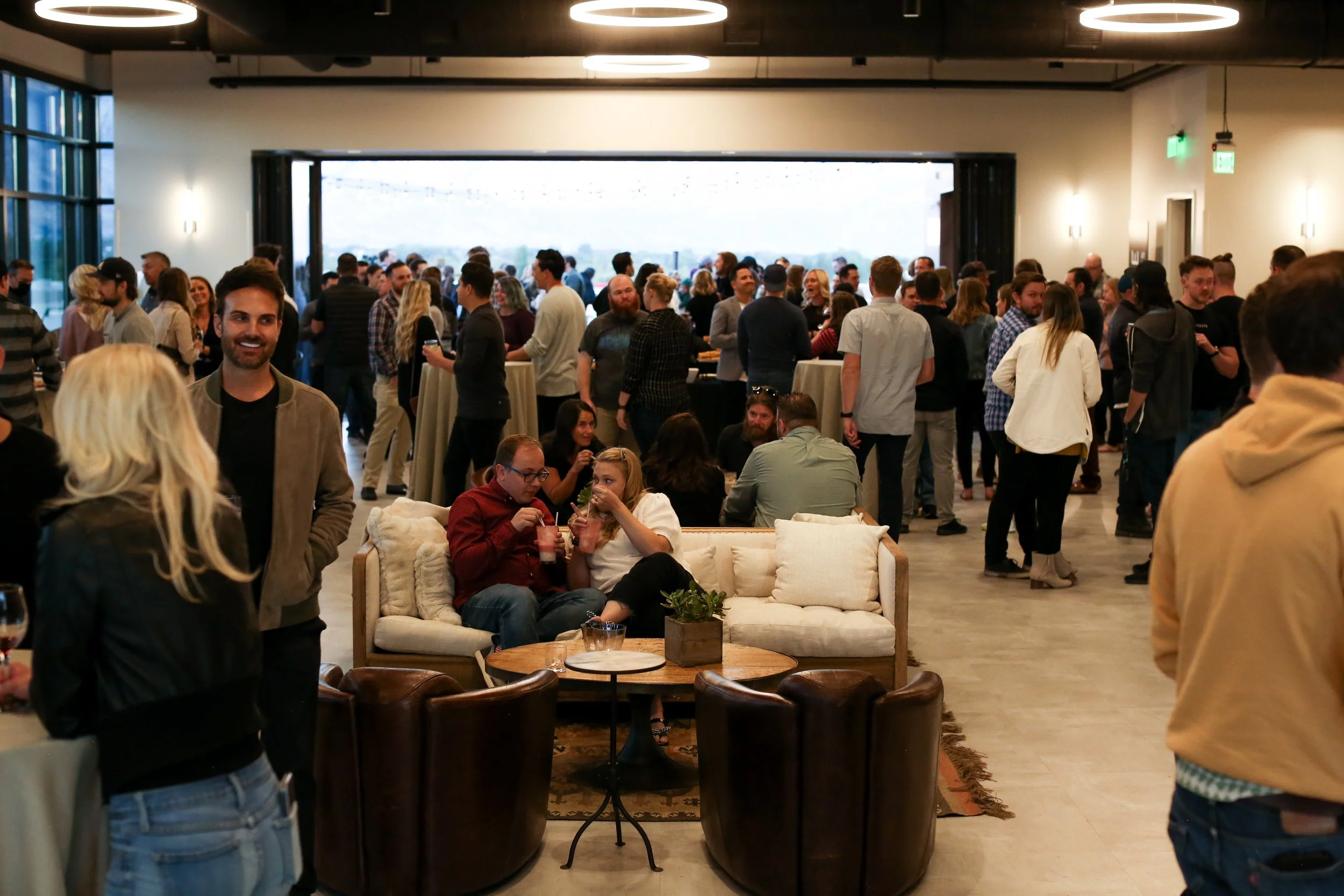 Several people are eating, drinking, and mingling in and indoor event venue.