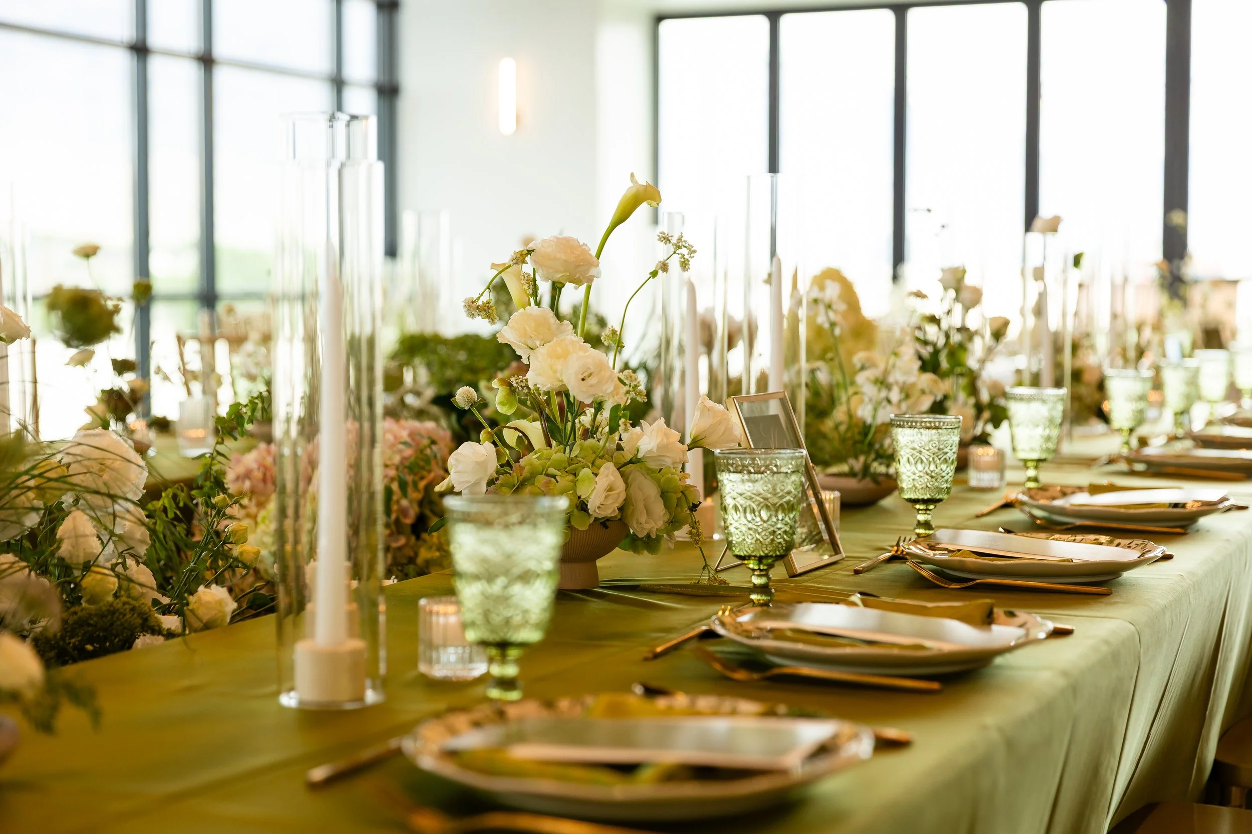 Rehearsal dinner setup green, white, and light pink florals between two tables.