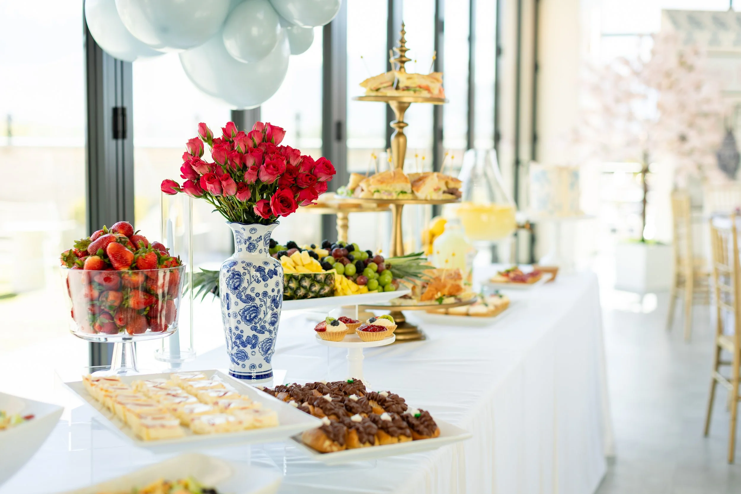 Bridal shower refreshment table with red roses, fruit, and eclairs.