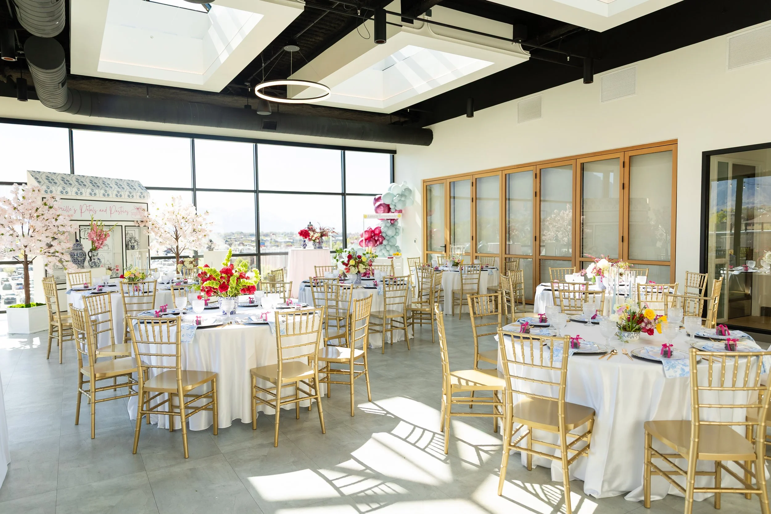 Bridal shower setup with round tables, gold chairs, white linens, and spring decor.