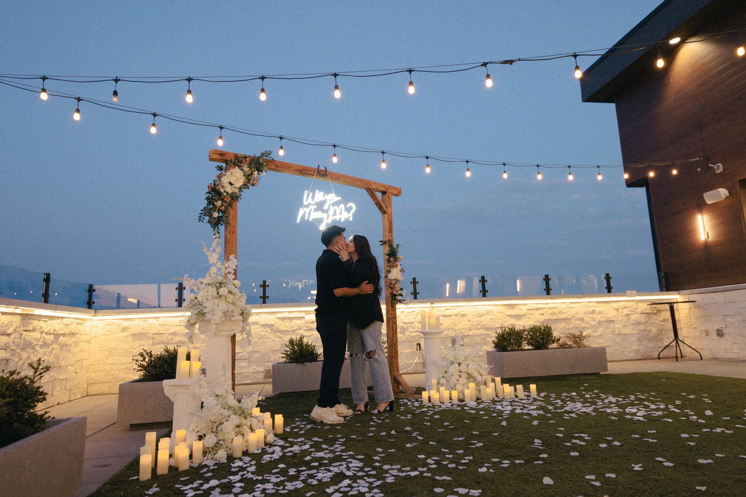 Man and woman kiss under a square arch in an outdoor courtyard.