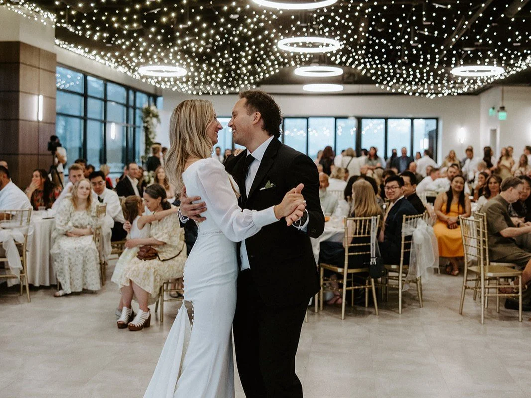 Bride and groom dance looking at each other in front of seated guests.