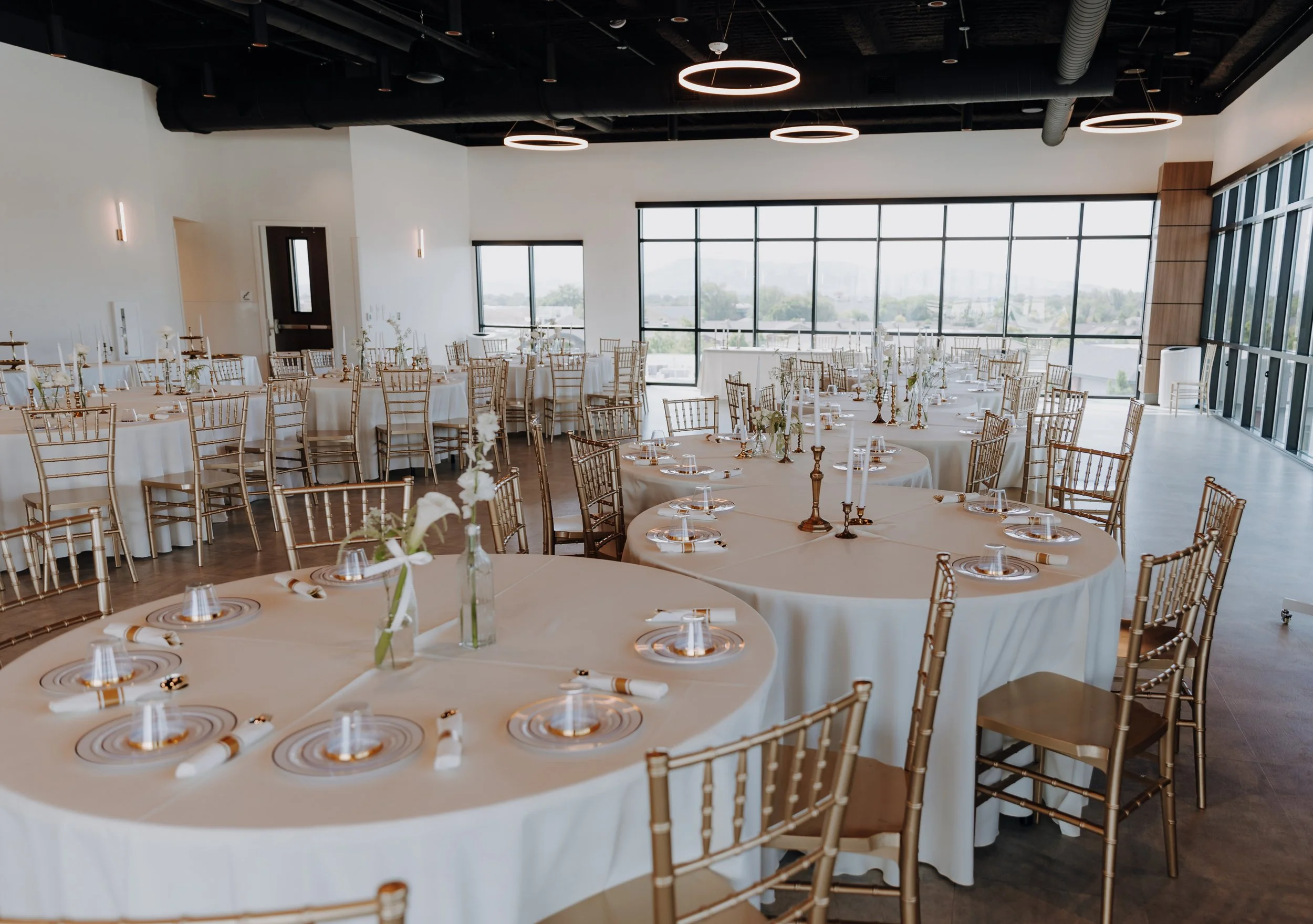 Round tables set up with gold chairs, white linens, and plating.