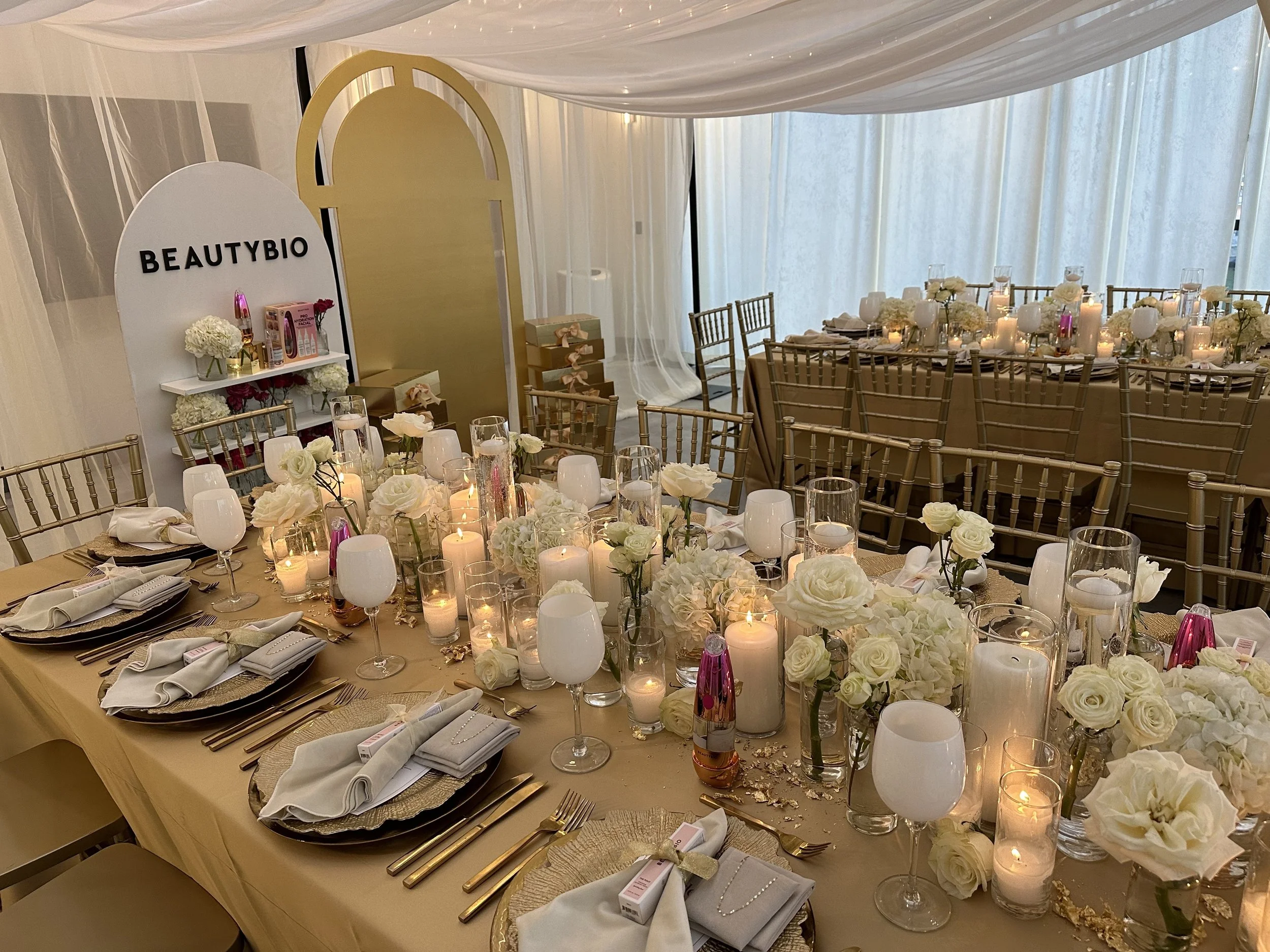 Formal dinner setup on long rectangle tables with gold linens, white flowers, and candles.