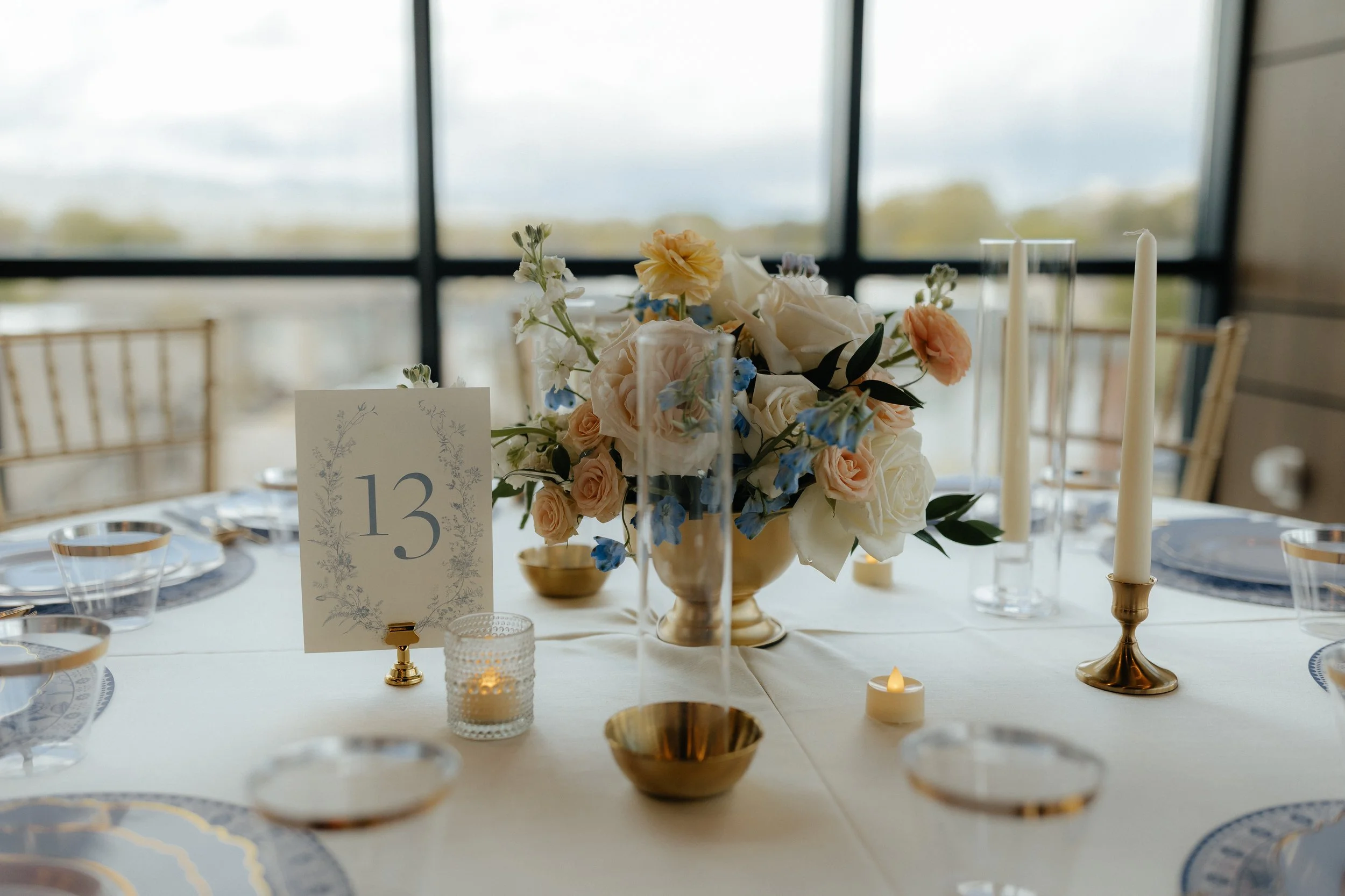 Wedding table setup with a floral centerpiece, cream colored candles, and table number card 13.