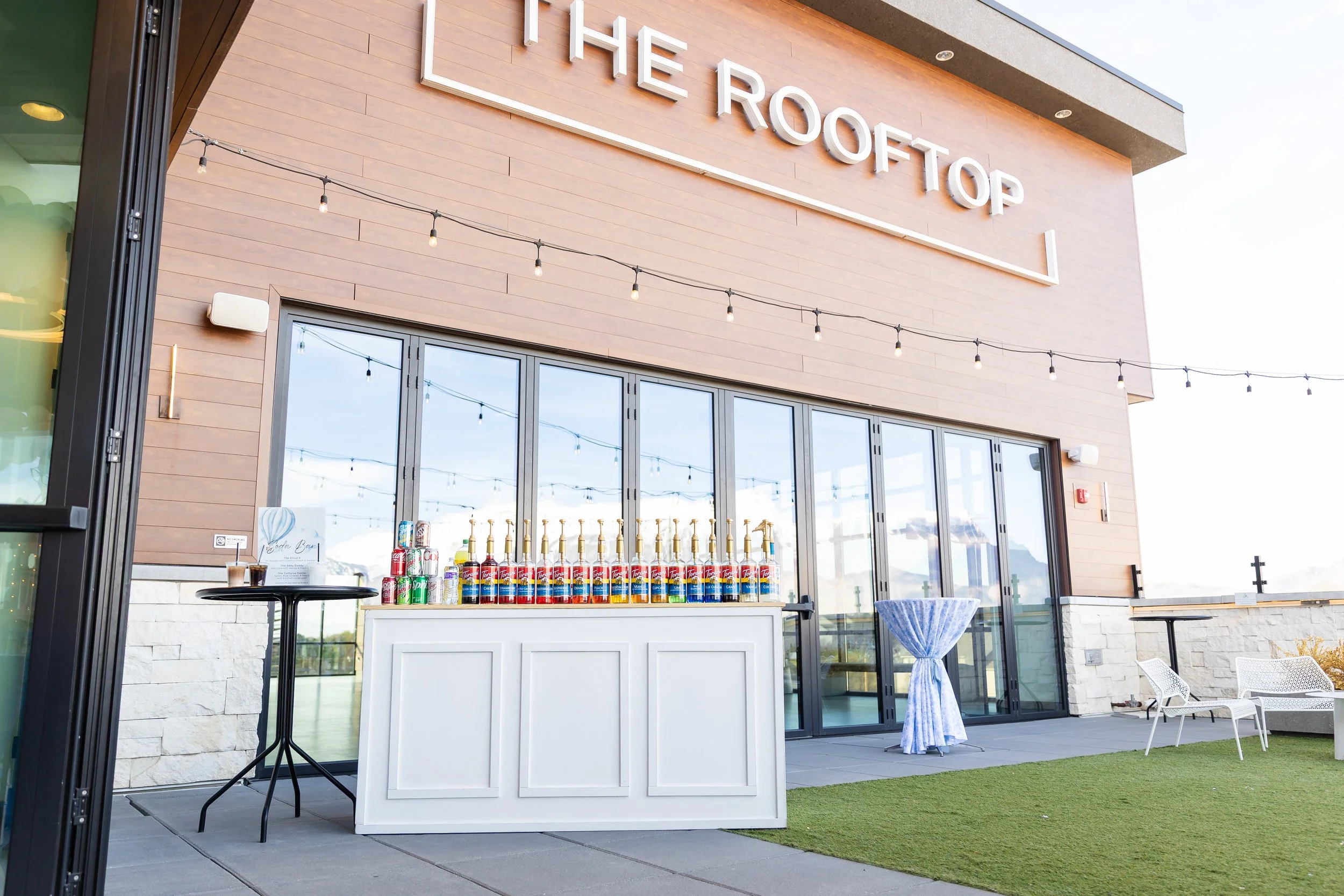A soda stations set up in the courtyard under the sign on the building that says THE ROOFTOP.