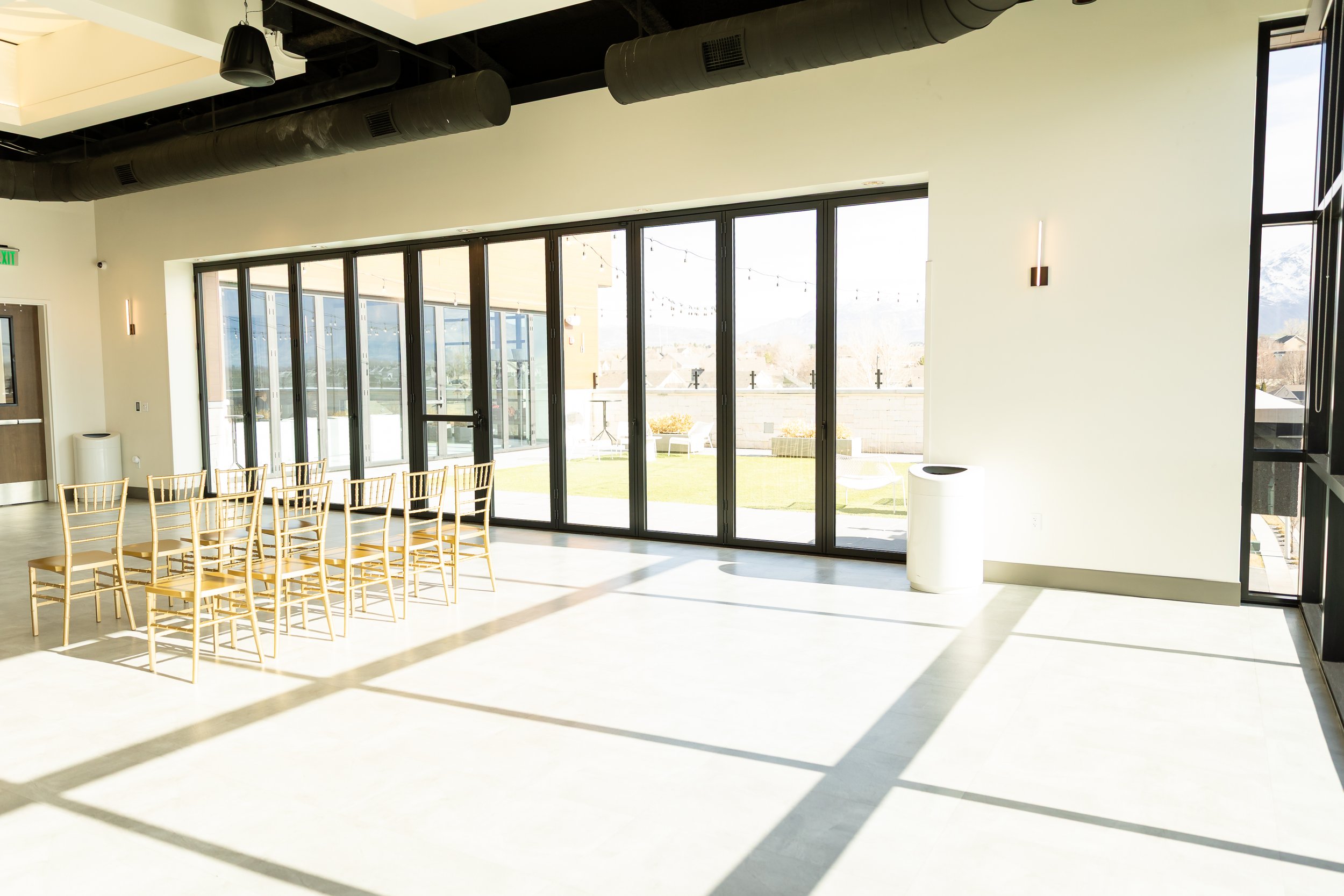 Large indoor venue space set up with gold chairs and looking into the courtyard through floor to ceiling windows.
