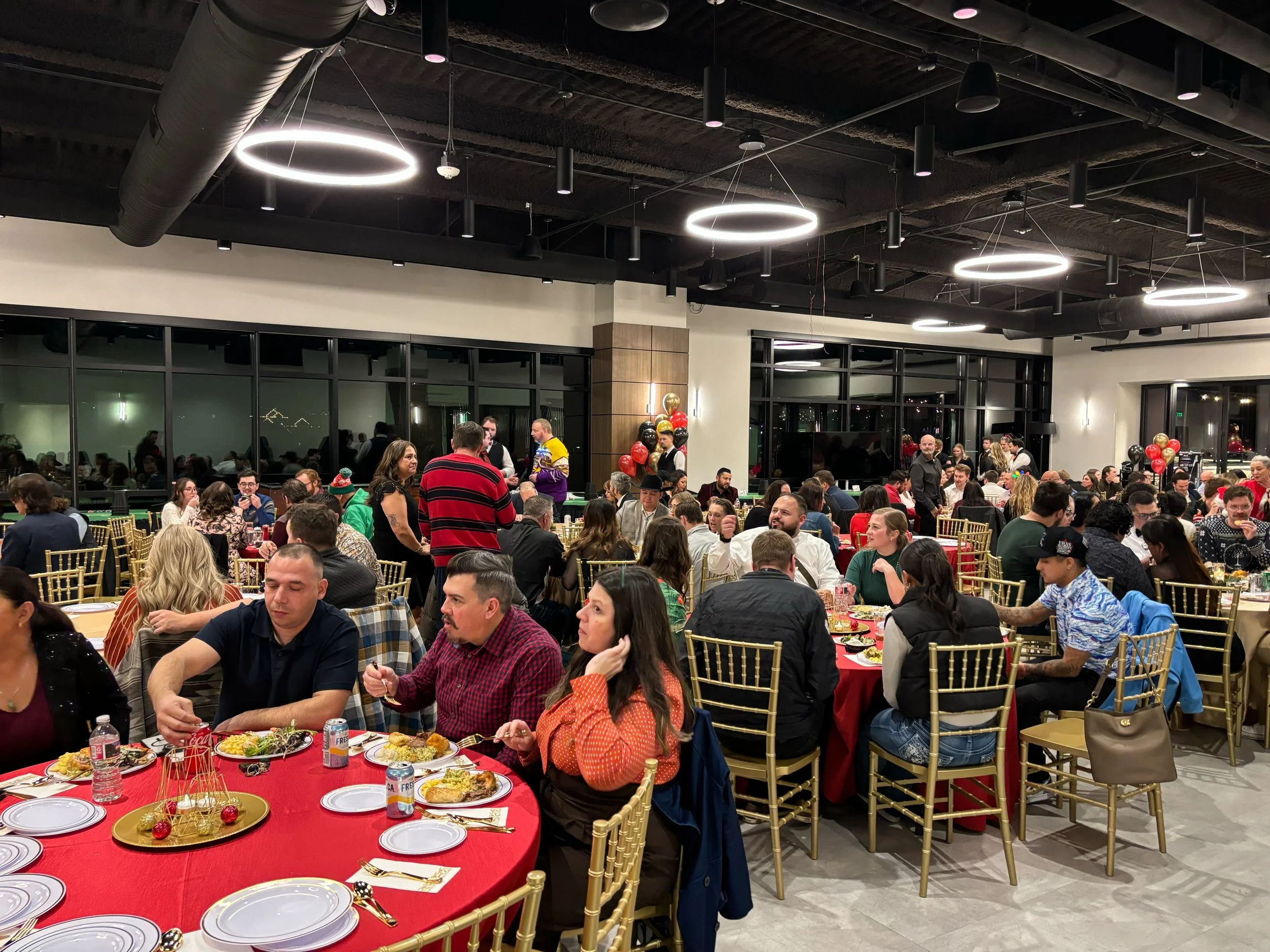 Groups of men and women sit around round tables eating a meal.