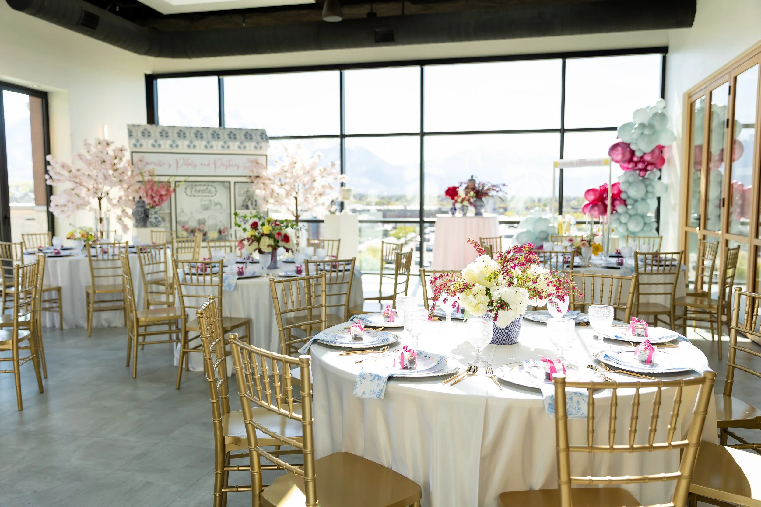 Bridal shower room setup with round tables, gold chairs, pink, white, and blue decorations.