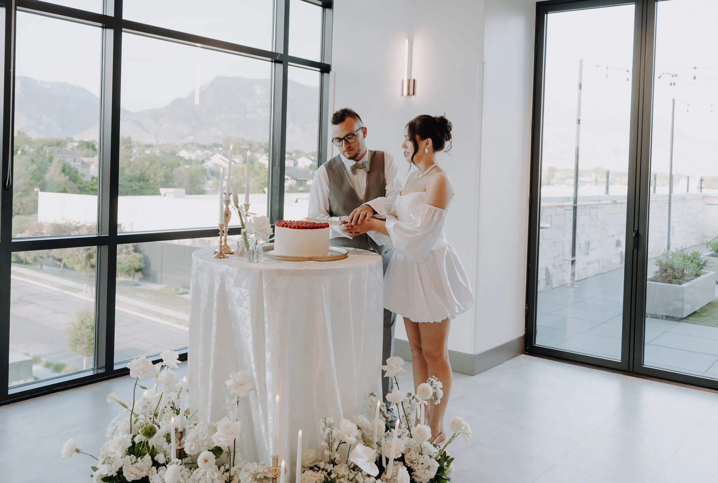 The bride and groom stand side by side and cut their white wedding cake together.