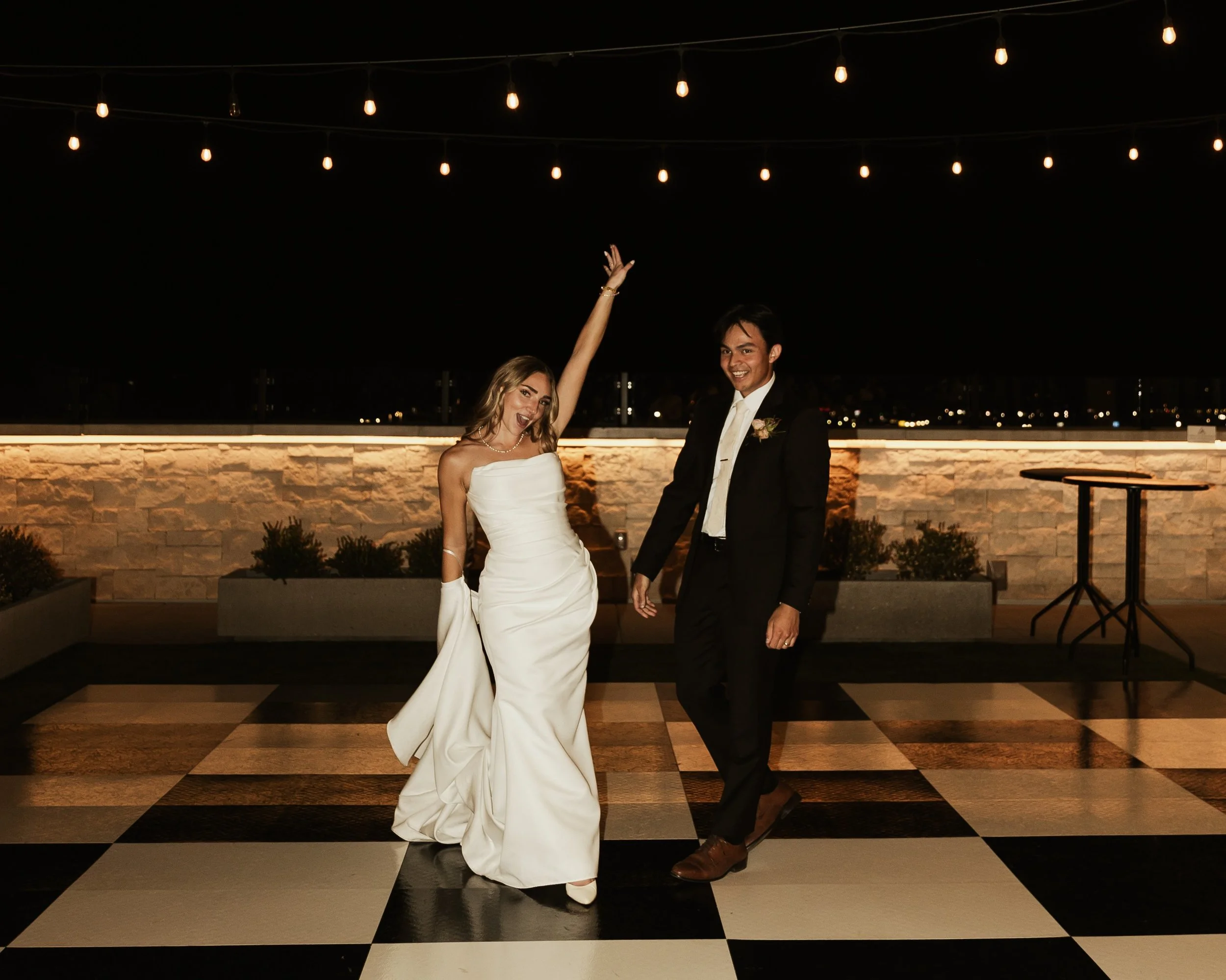 Bride and groom stand on a black and white checkered dance floor in the outdoor courtyard.