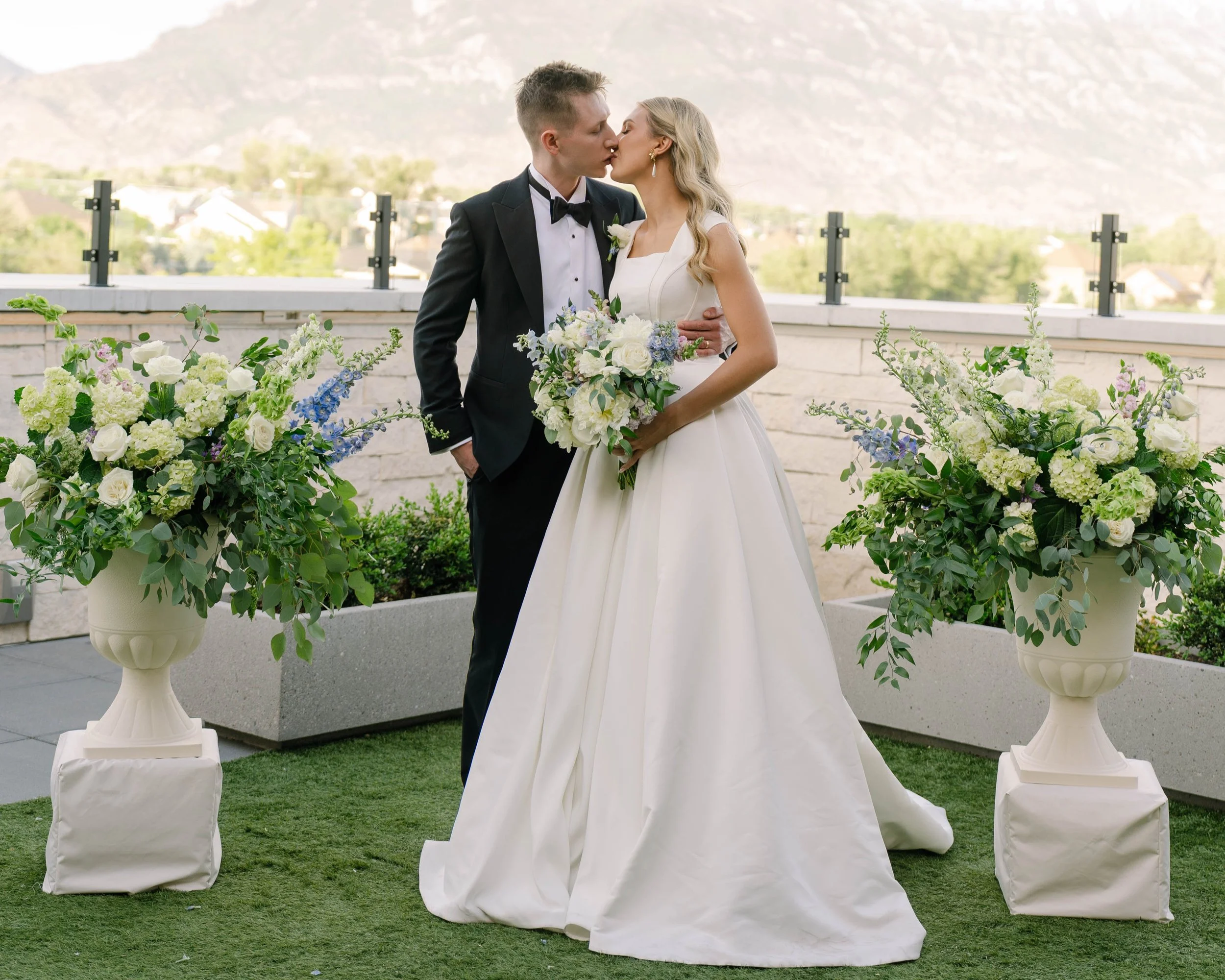 Bride and groom kiss in the courtyard in between two large floral arrangements.