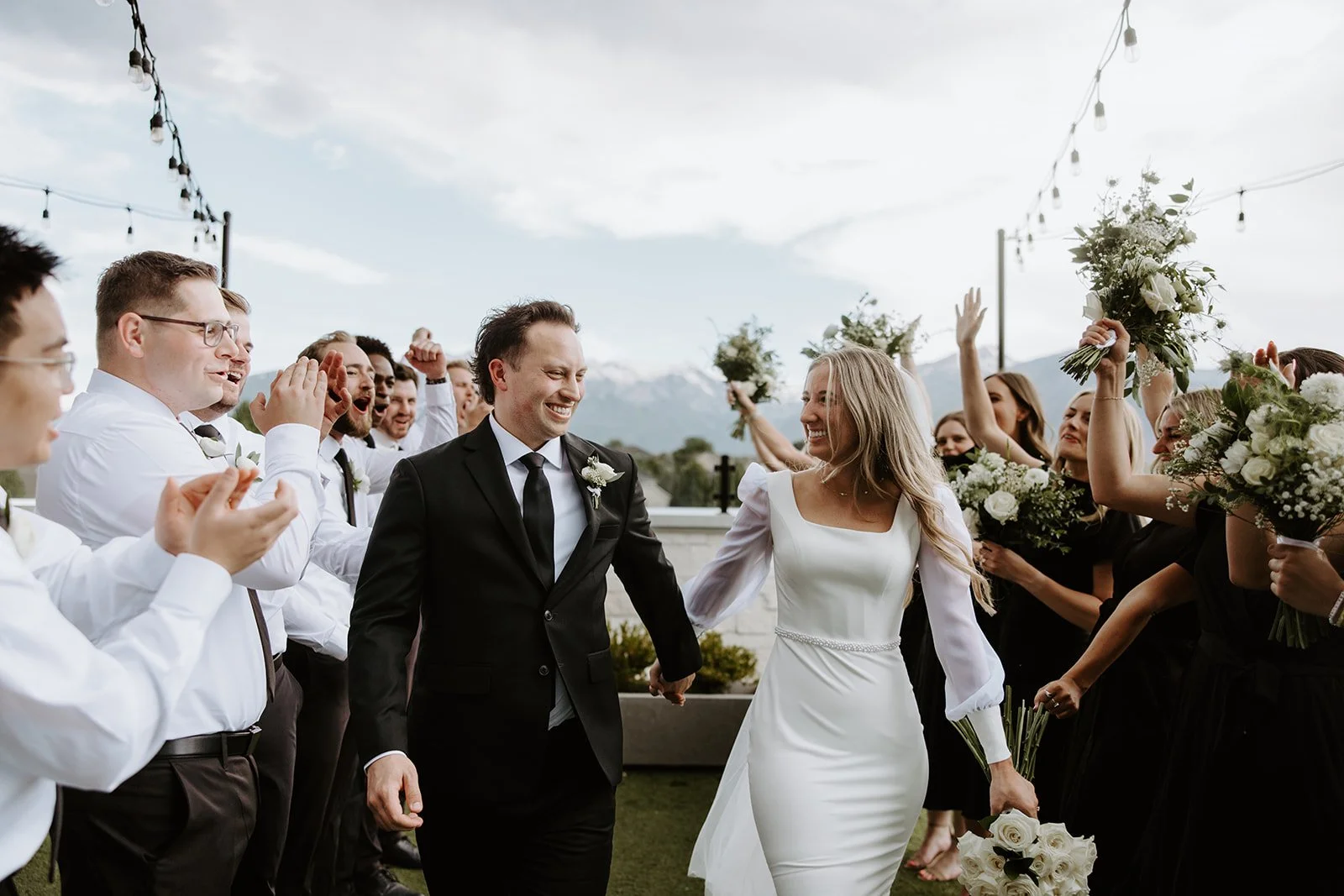 Bride and groom walk holding hands down an aisle created by the wedding party.
