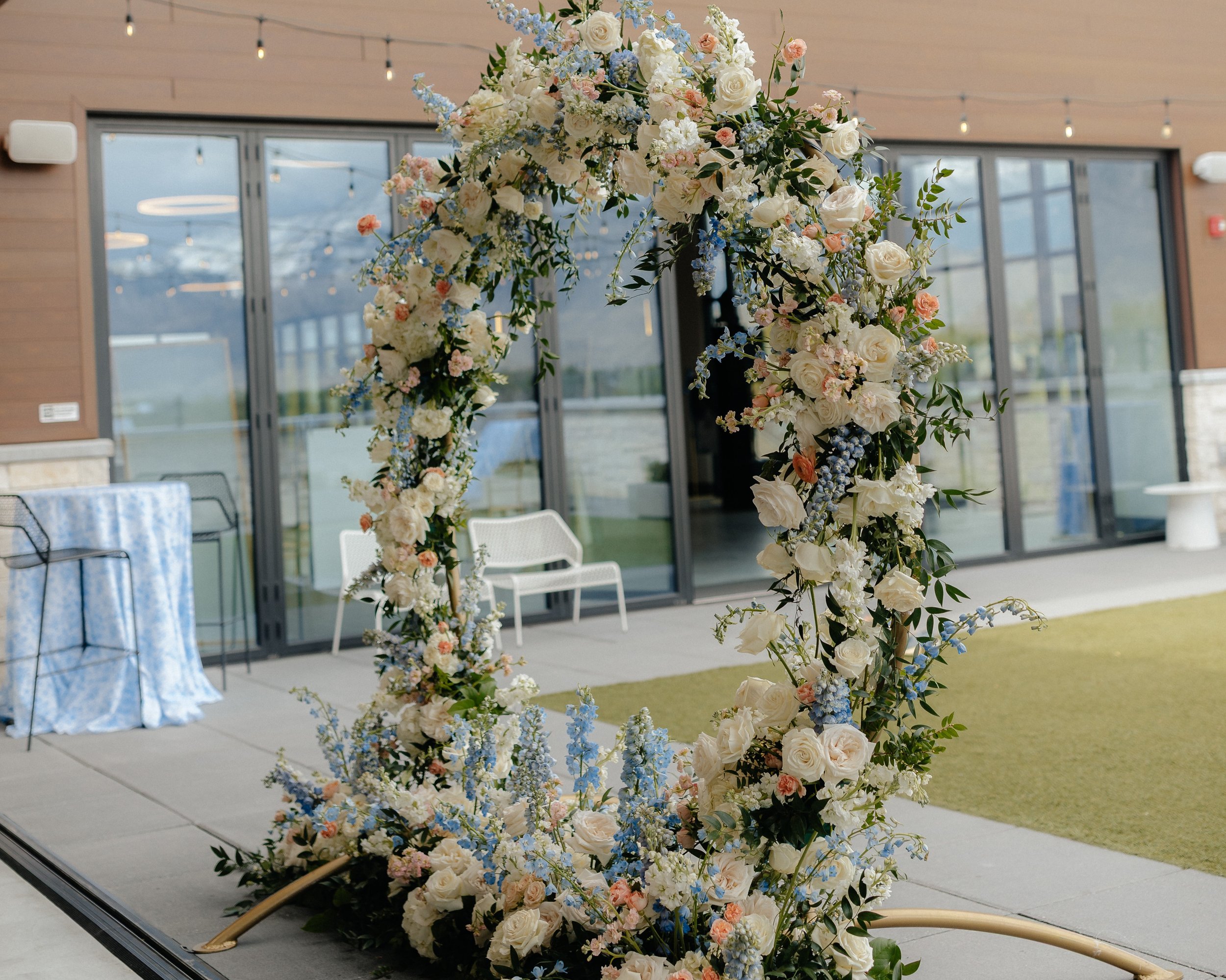 Circular wedding arch covered with flowers that are white, blue, and peach colored.
