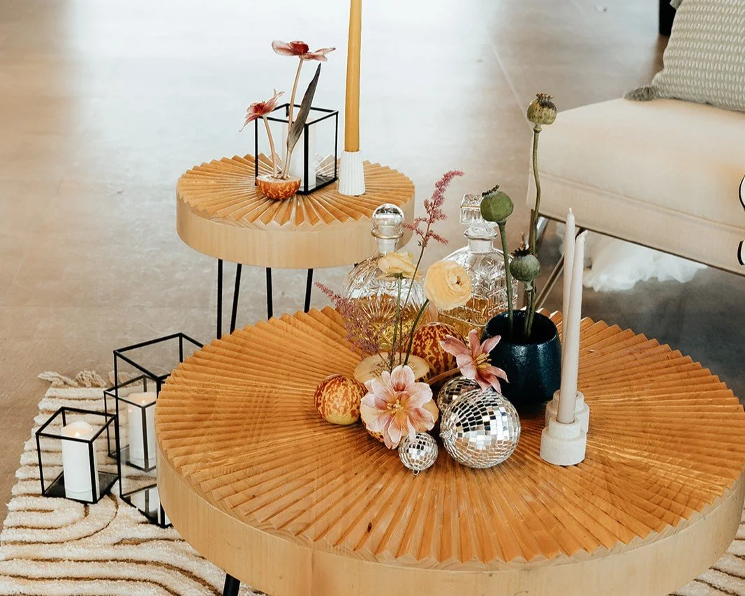 Two small round wooden tables setup for a photoshoot with small disco balls, candles, and some flowers placed on top of the tables.