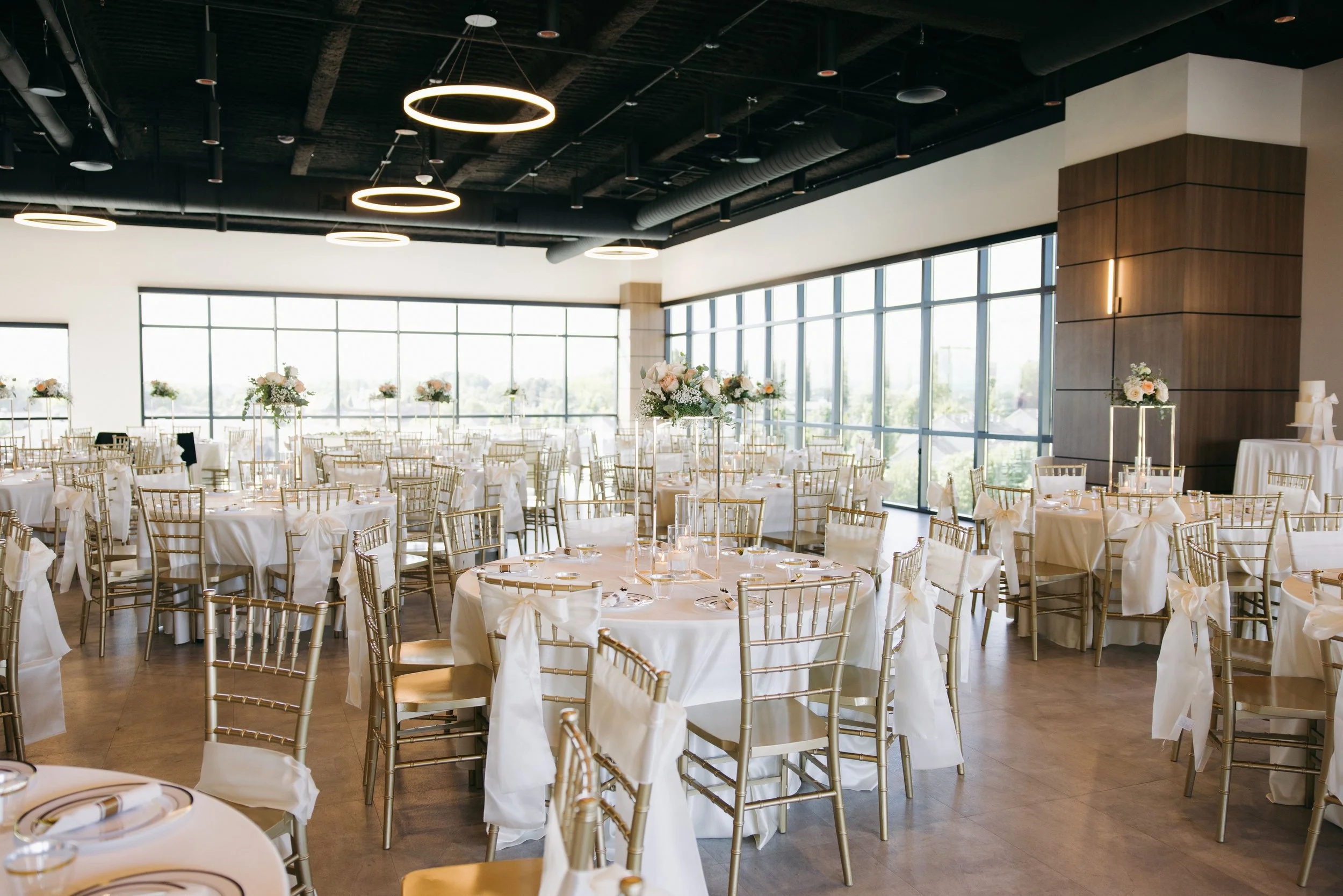Indoor venue setup with round tables covered with white linens and tall floral arrangements.