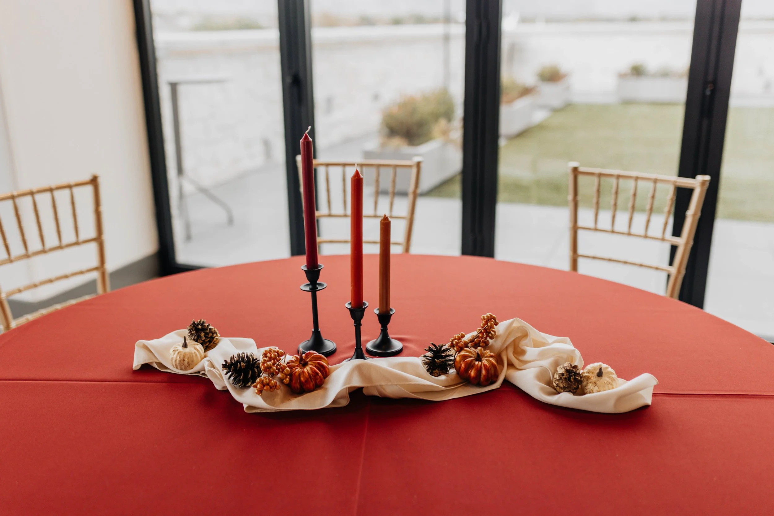 A round table decorated with a dark orange linen, little pumpkins, black candlesticks, and orange candles.