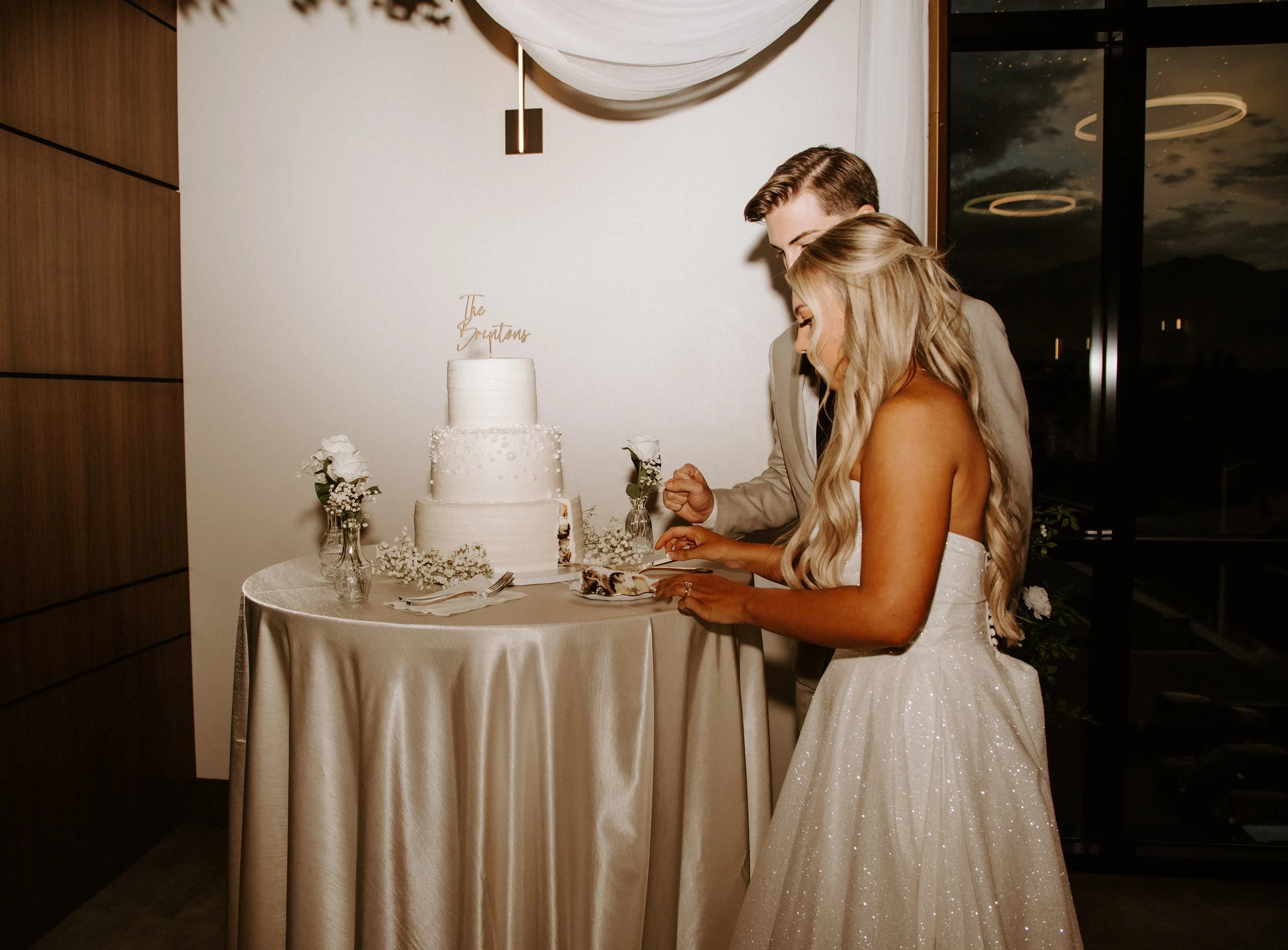 Bride and groom cut a white three-tiered wedding cake.