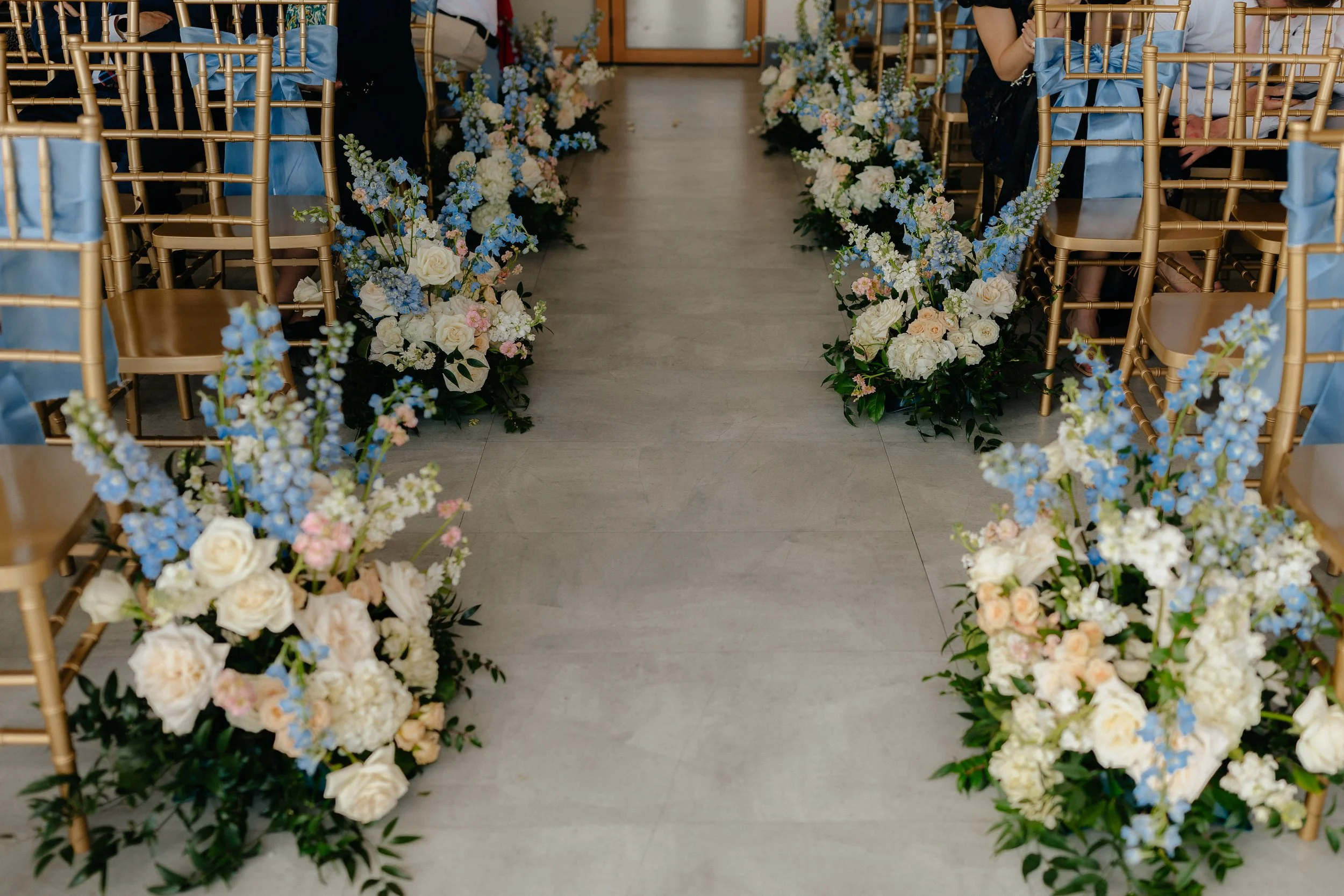 Floral arrangements are placed at the end of each row of chairs with blue, white, and pink flowers.