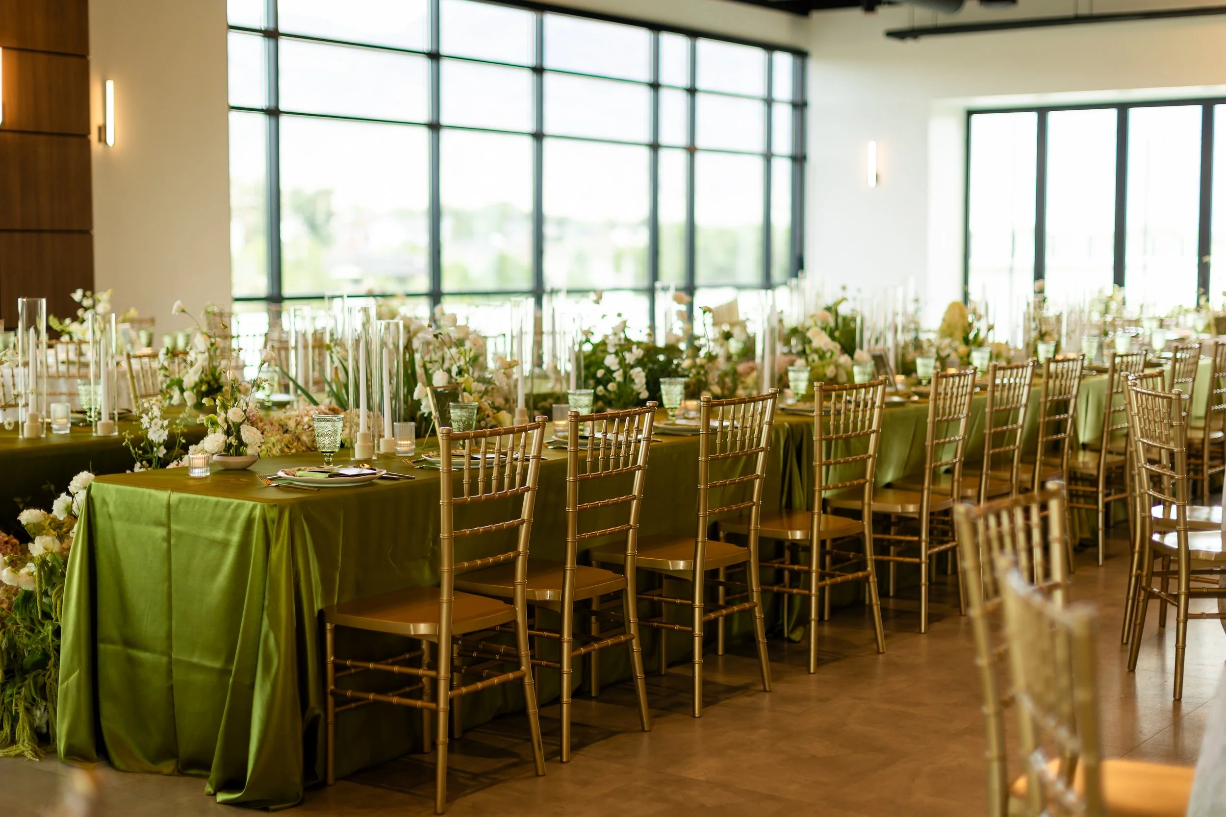 Rehearsal dinner setup with long tables, lime green linens, gold chairs, lush florals, and candles.