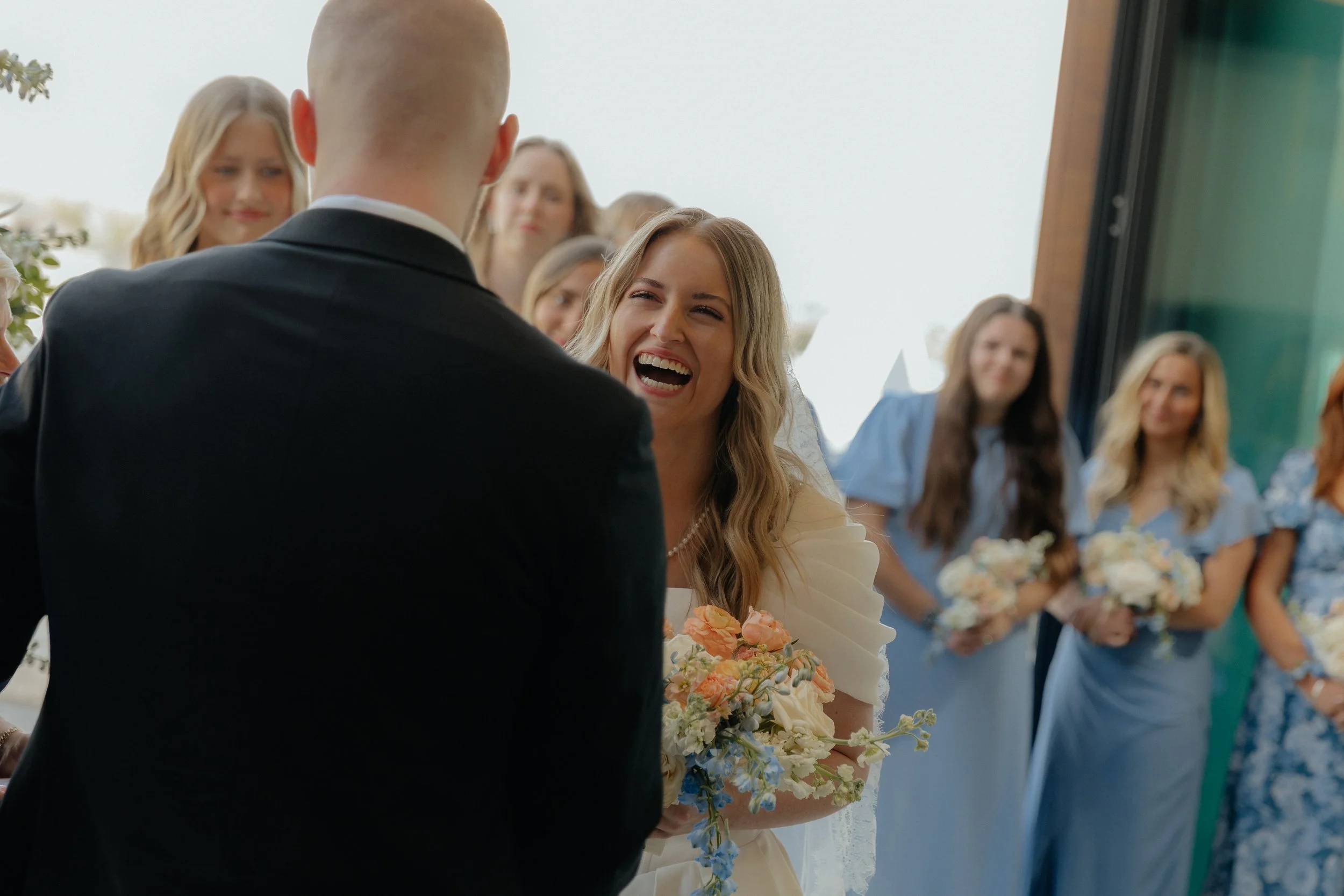 Bride is smiling at the groom with her bridesmaids in blue standing behind her.