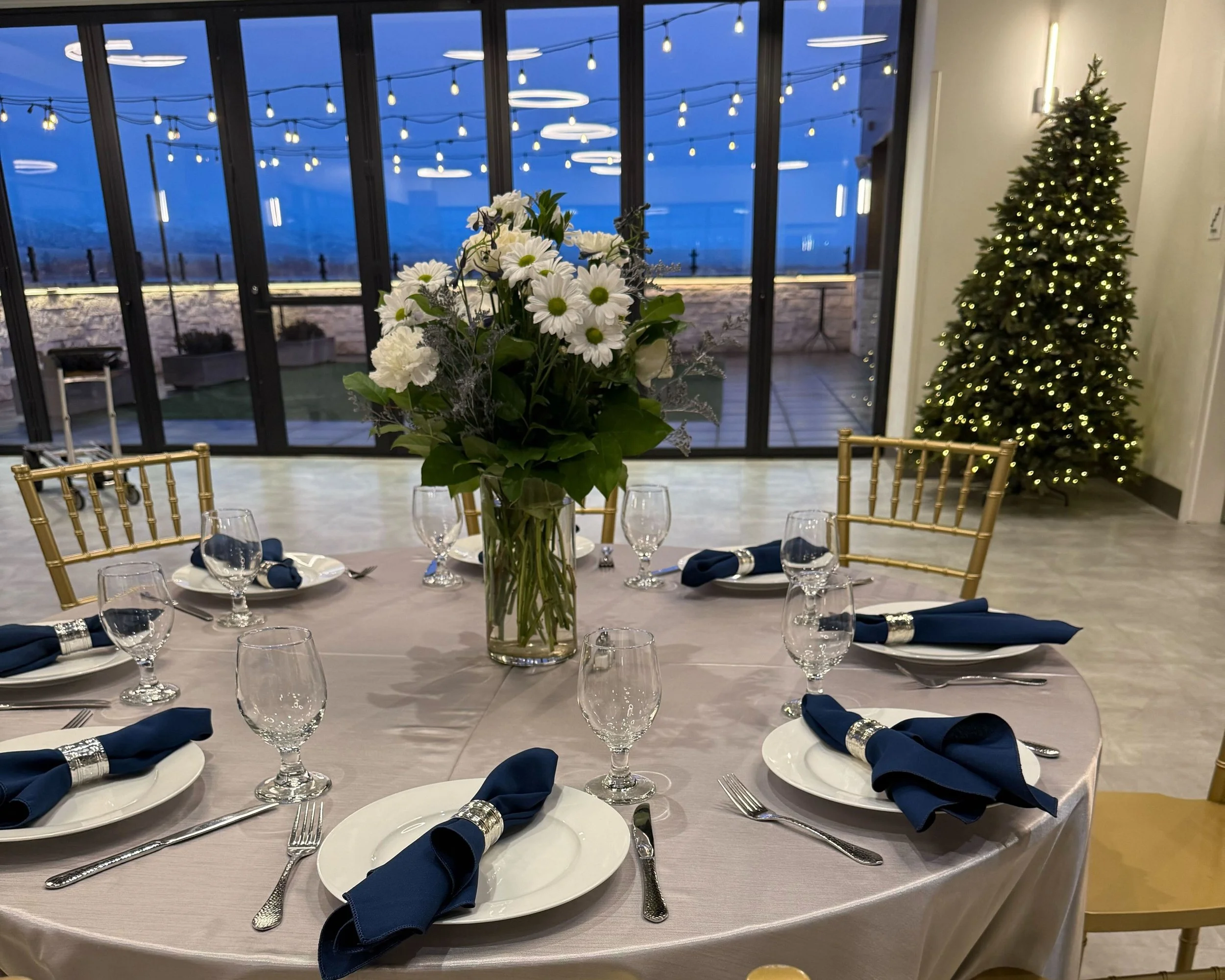Round table setup with silver tablecloth, white plates, and a bouquet of white flowers as the centerpiece.