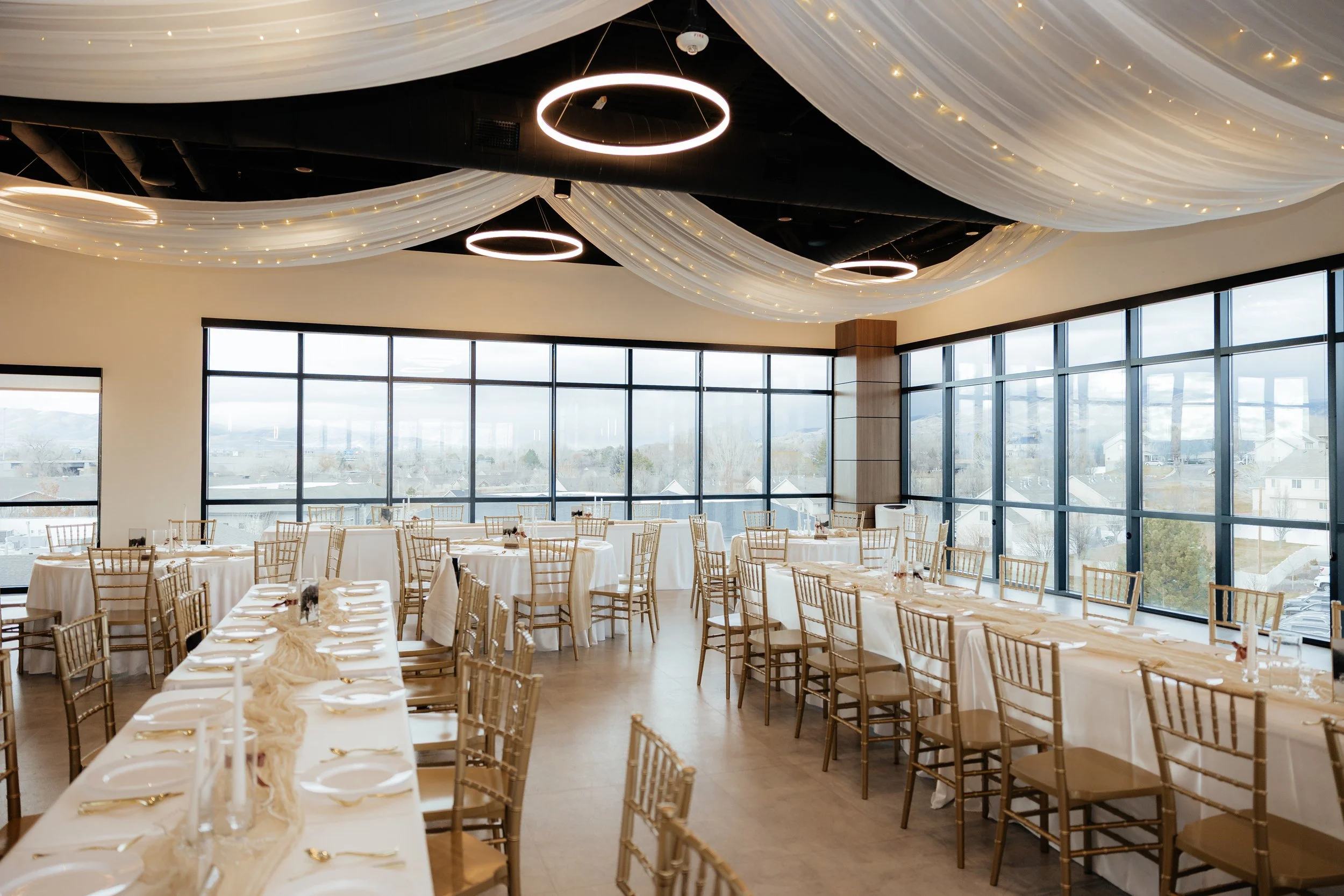 Long wedding tables setup with ivory linens, white plates, and gold flatware.
