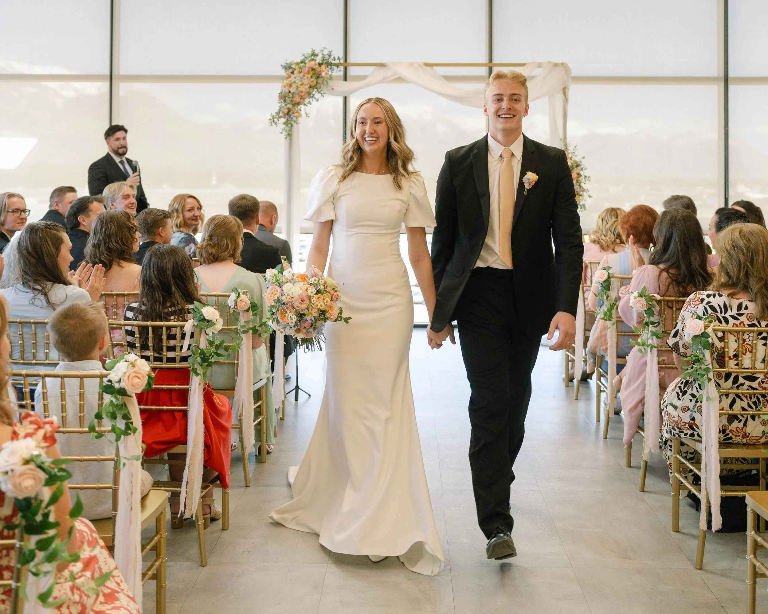 Bride and groom walk hand in hand down the indoor wedding aisle.