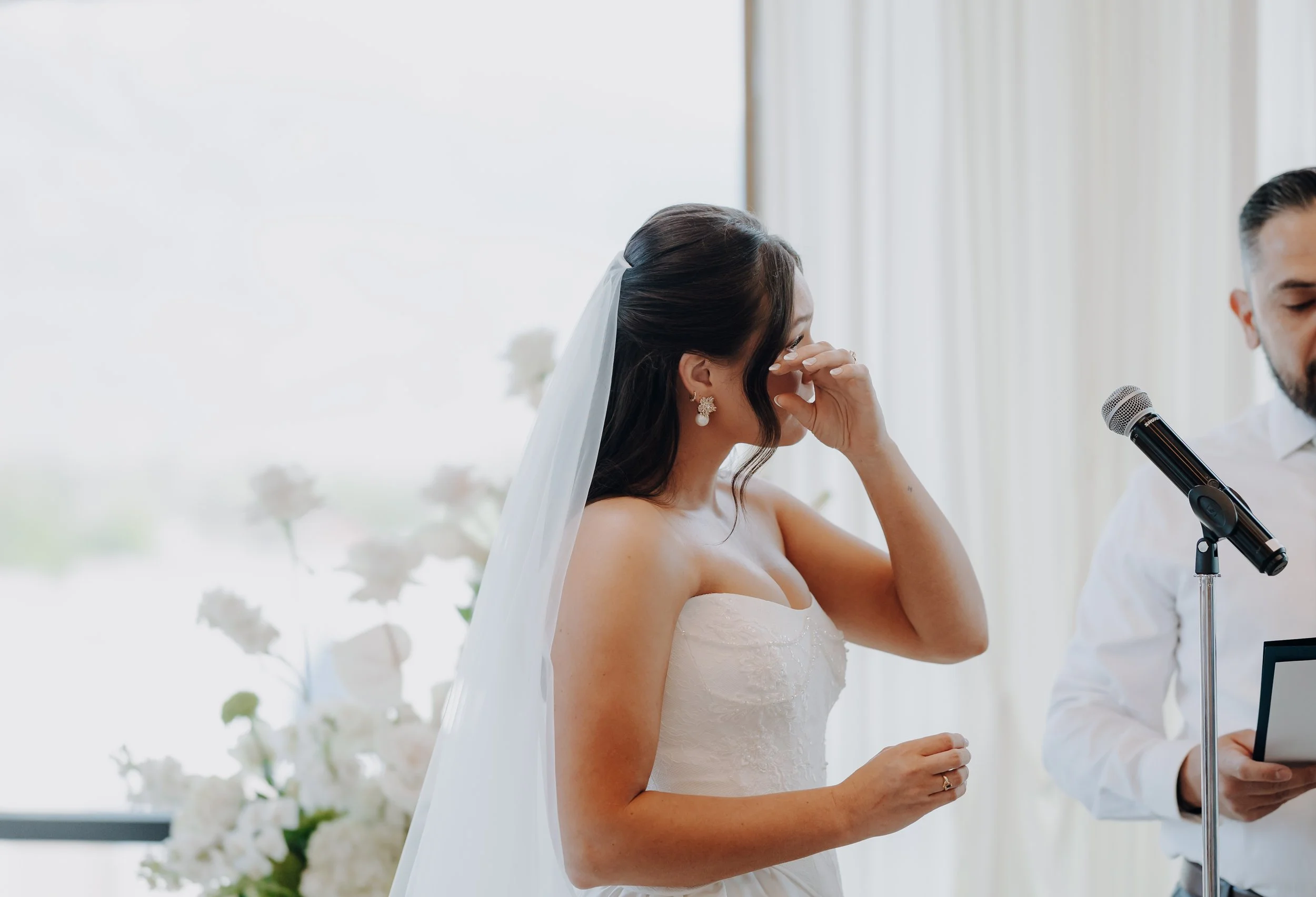 Bride wipes a tear from her eyes during wedding ceremony.