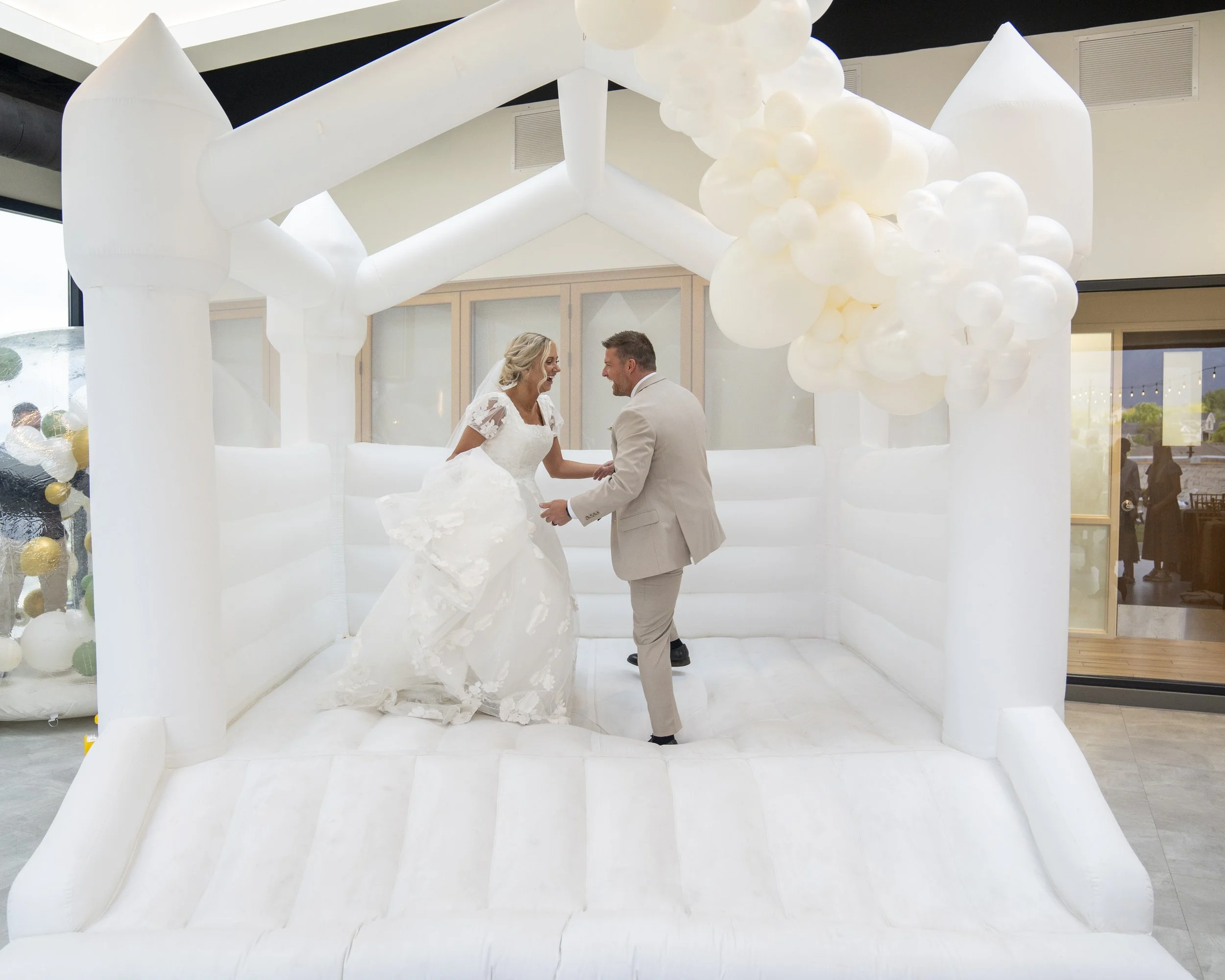 Bride and groom jump in a white bounce house while wearing their wedding attire.