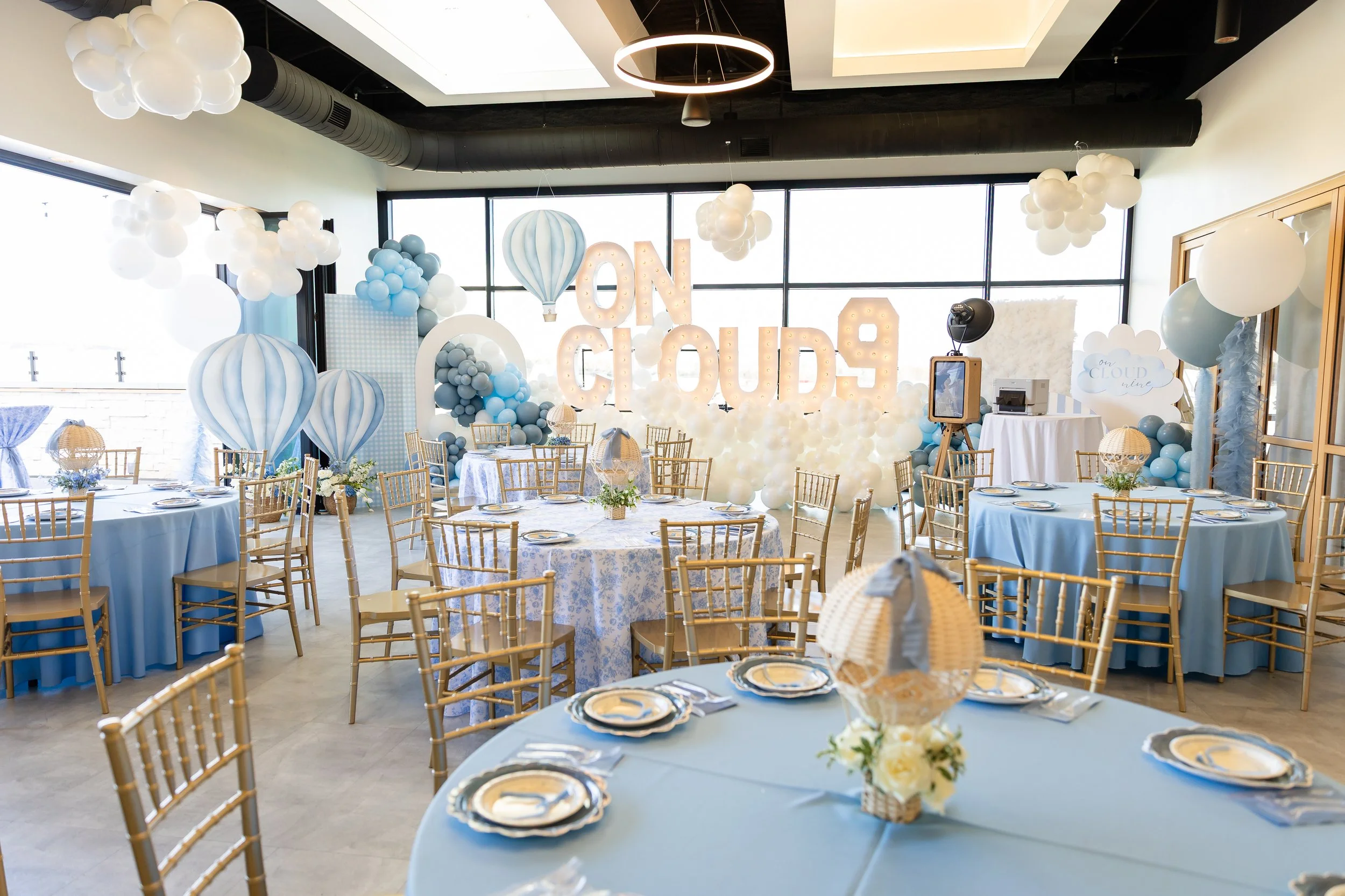 Large indoor venue space with round tables covered in blue linens set up and marquee letters that spell out ON CLOUD 9.