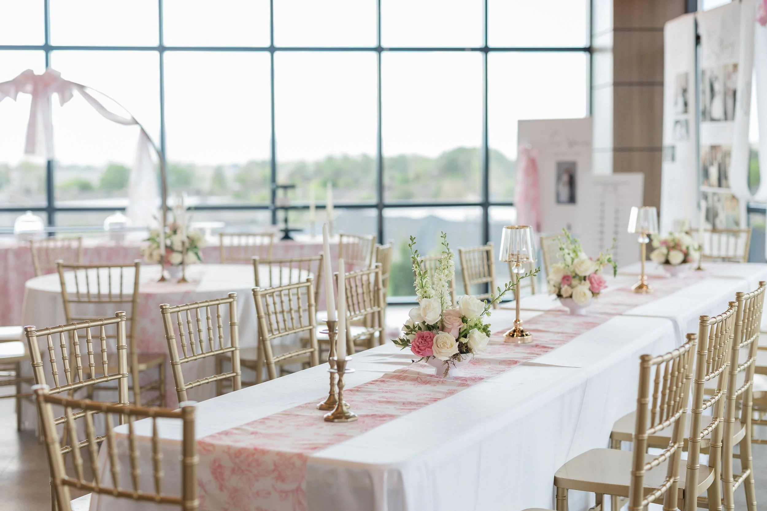 Rectangle table decorated with pink runners, flowers, candles, and small lamps.