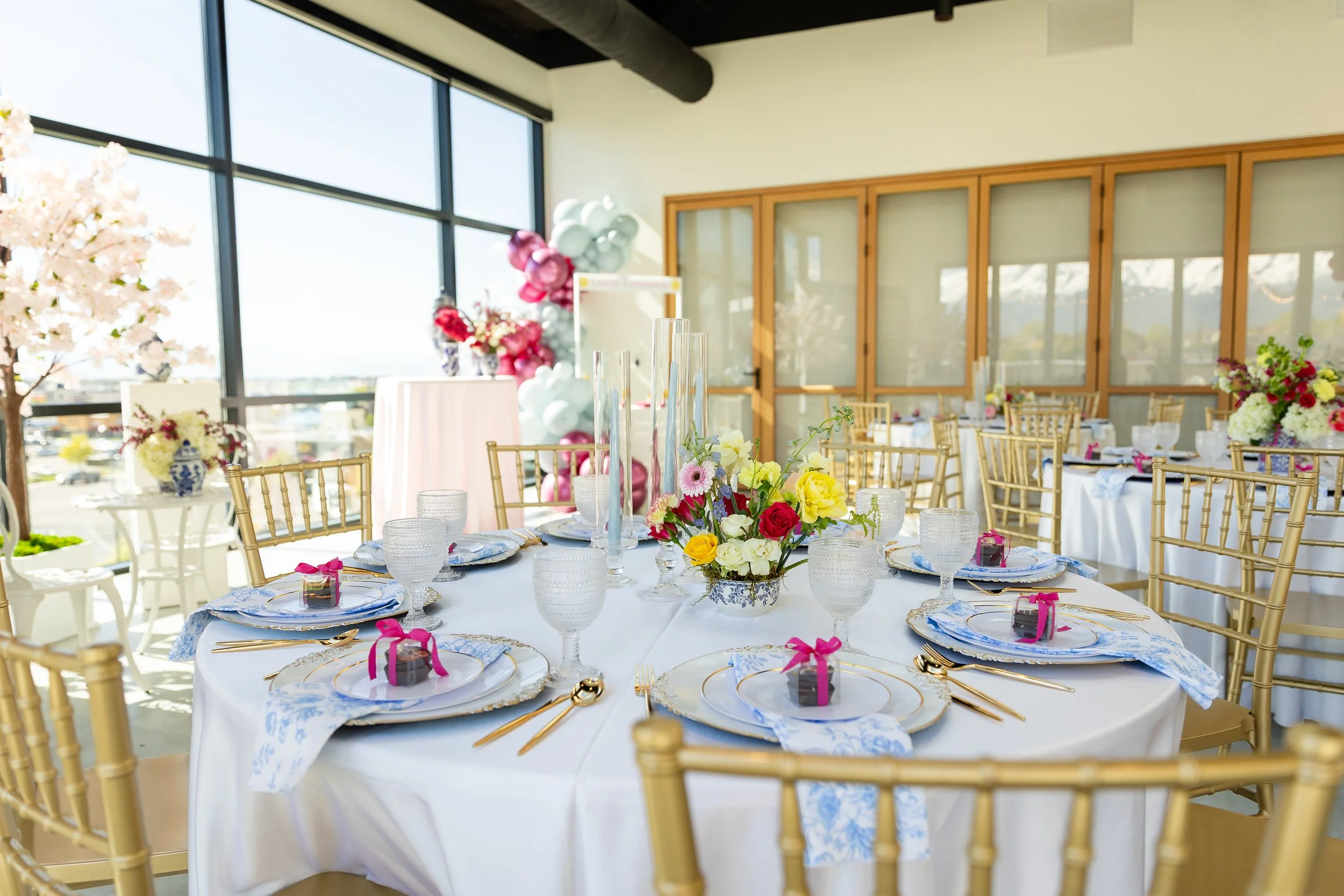 Round table setup for a bridal shower with flowers, plating, and a little present on each plate.