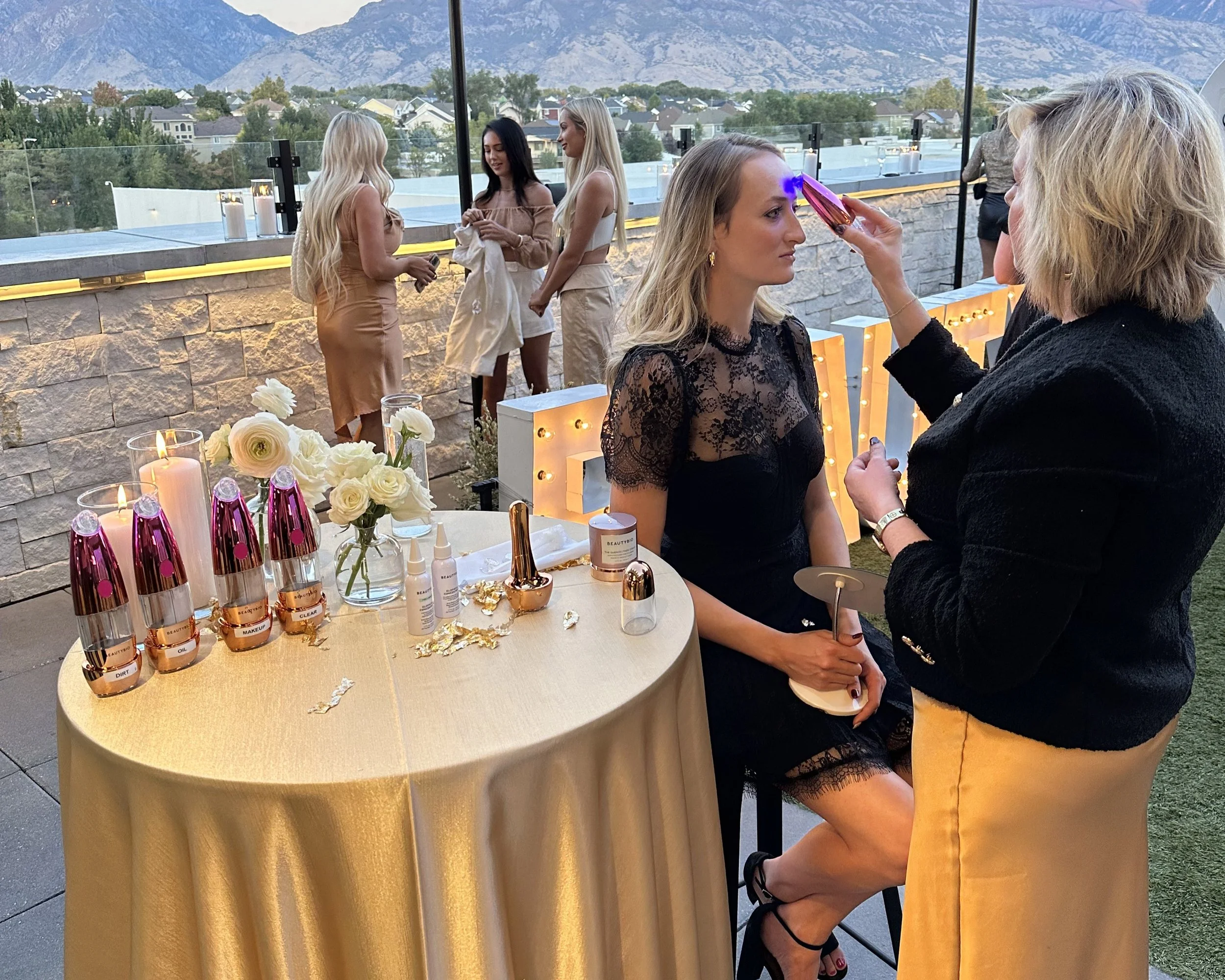 Women sits in a bar chair while another woman demonstrates a skin care tool.