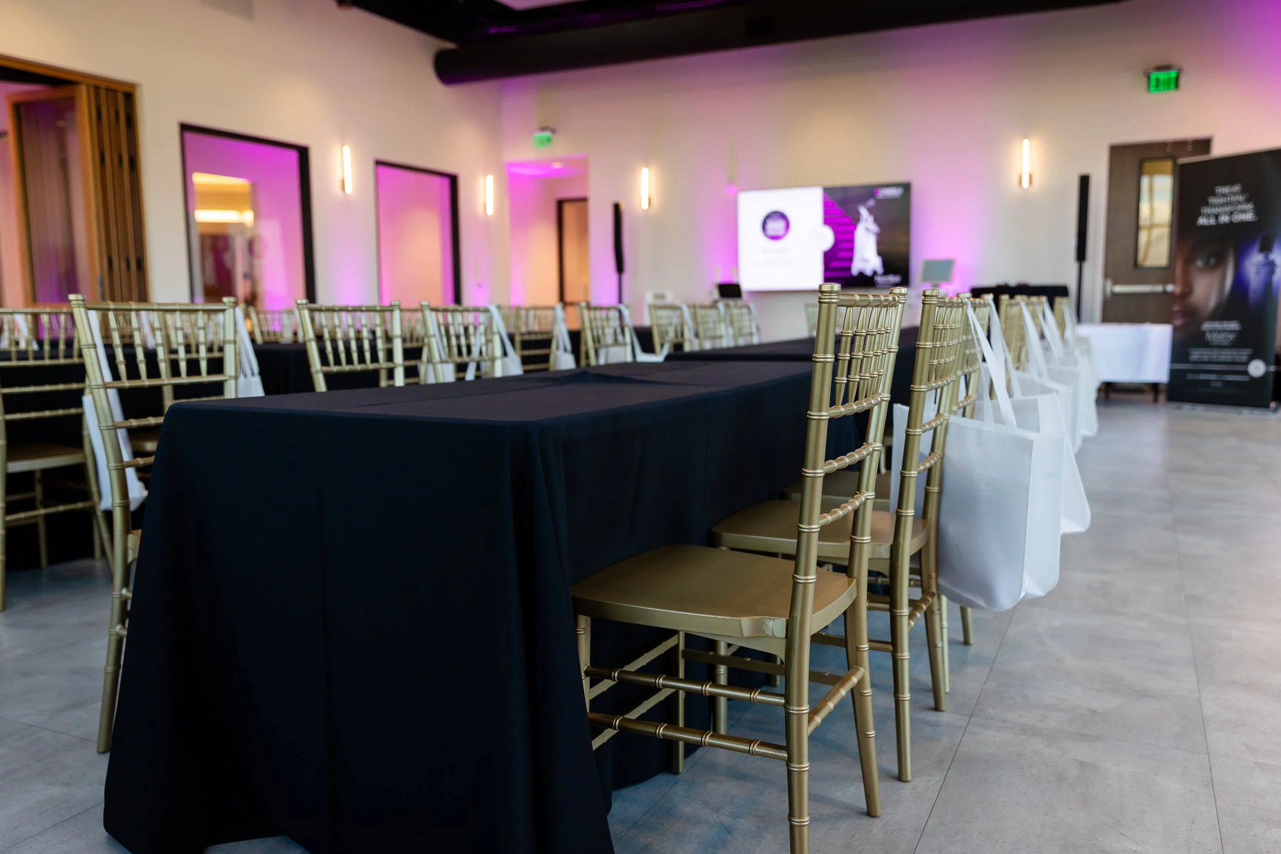Rectangle tables setup with black linens and gold chairs around each table.