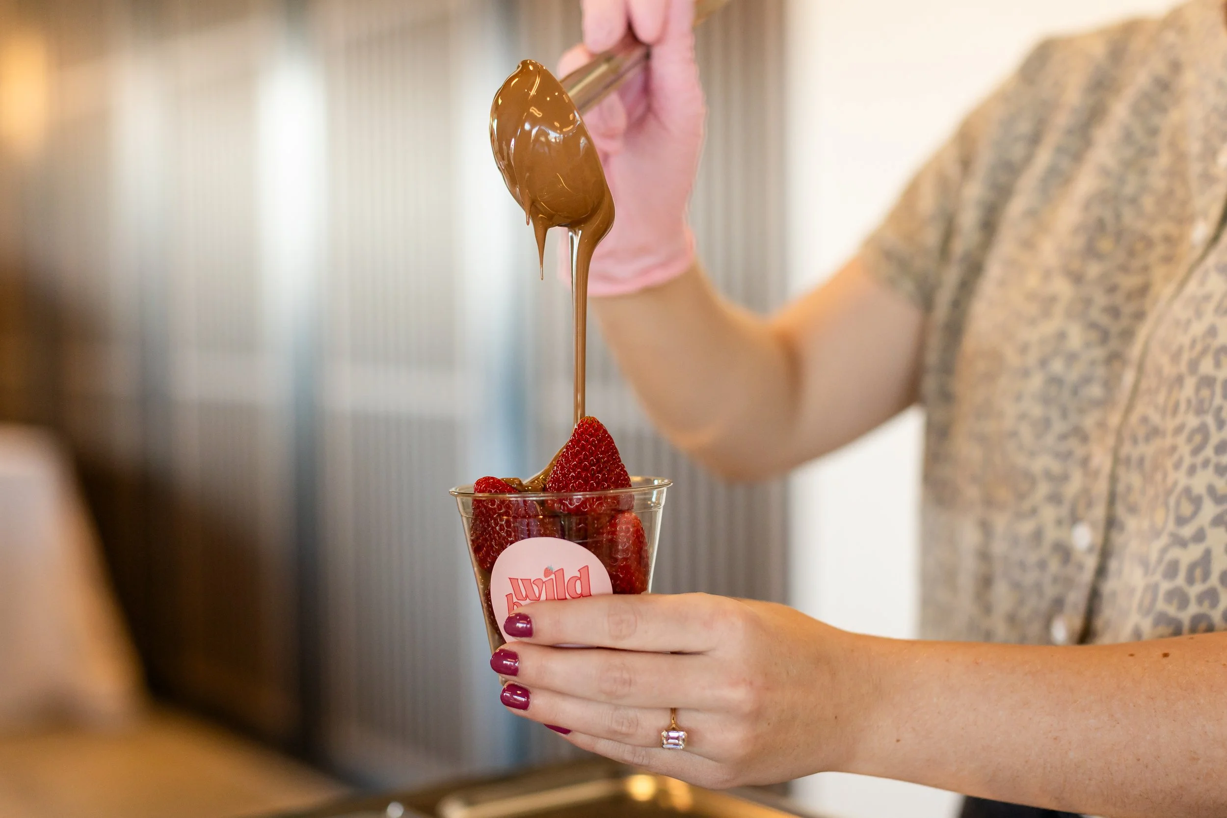 Caterer drizzles chocolate syrup over a cup of strawberries.