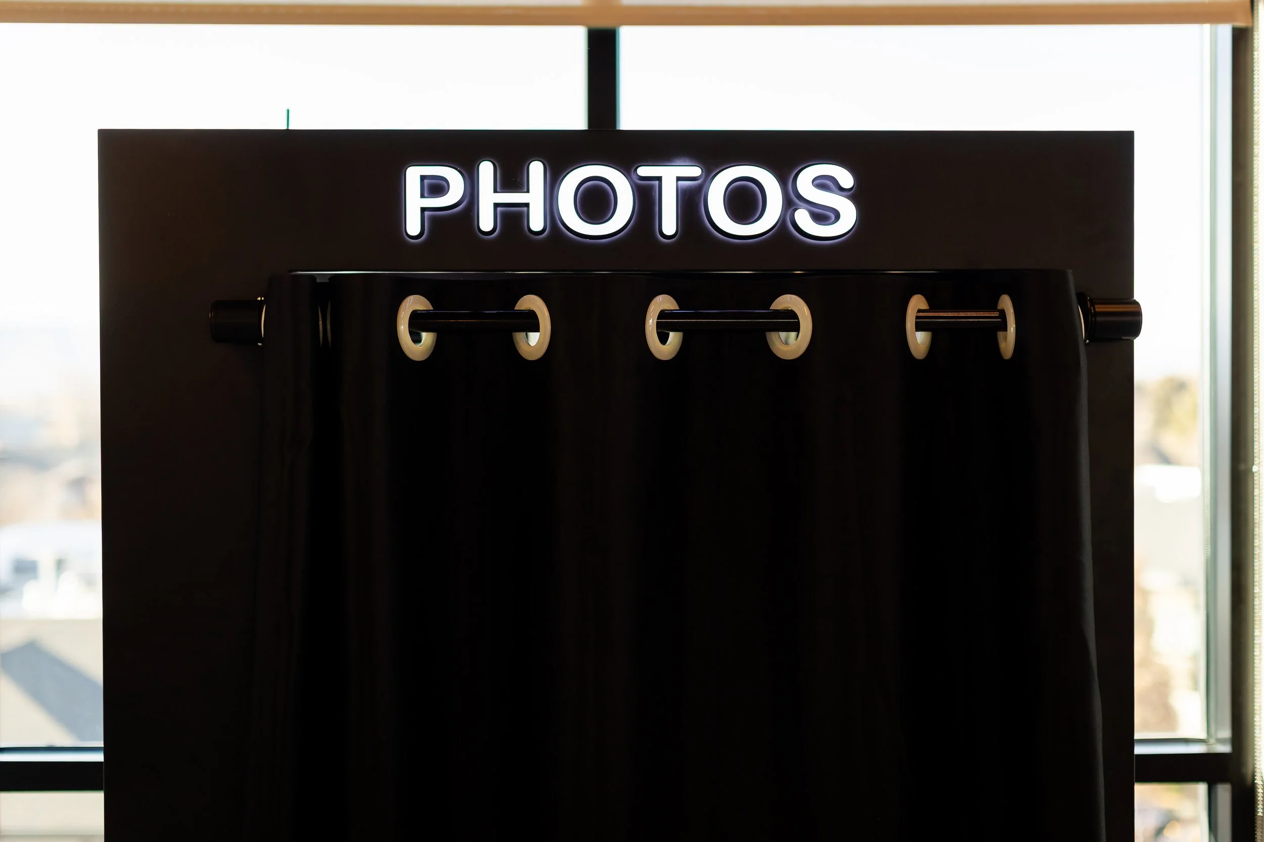 The top of a black photo booth that has the word "photos" in LED letters at the top.