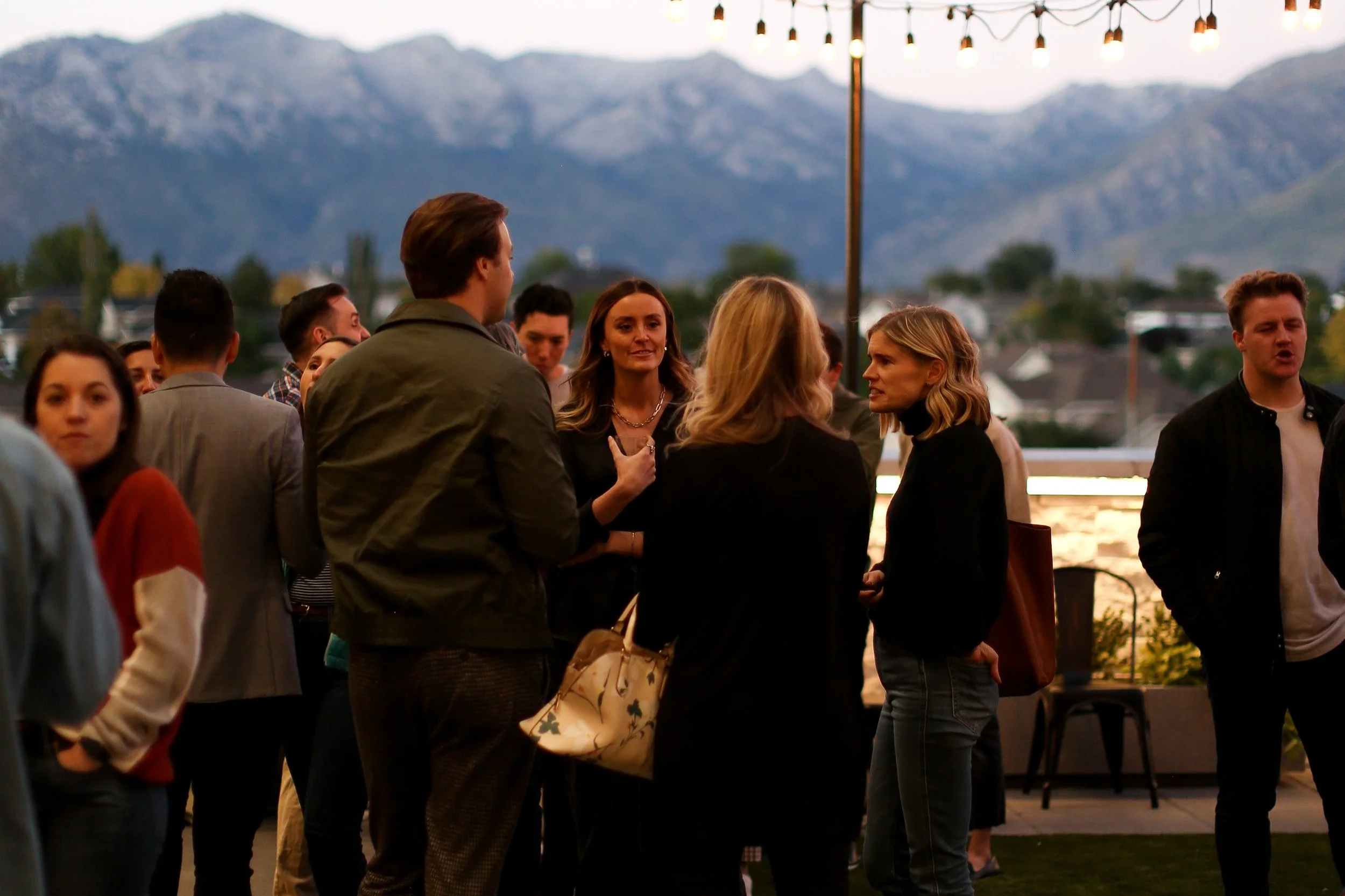 Several adults talk outside in the courtyard with a mountain view behind them.