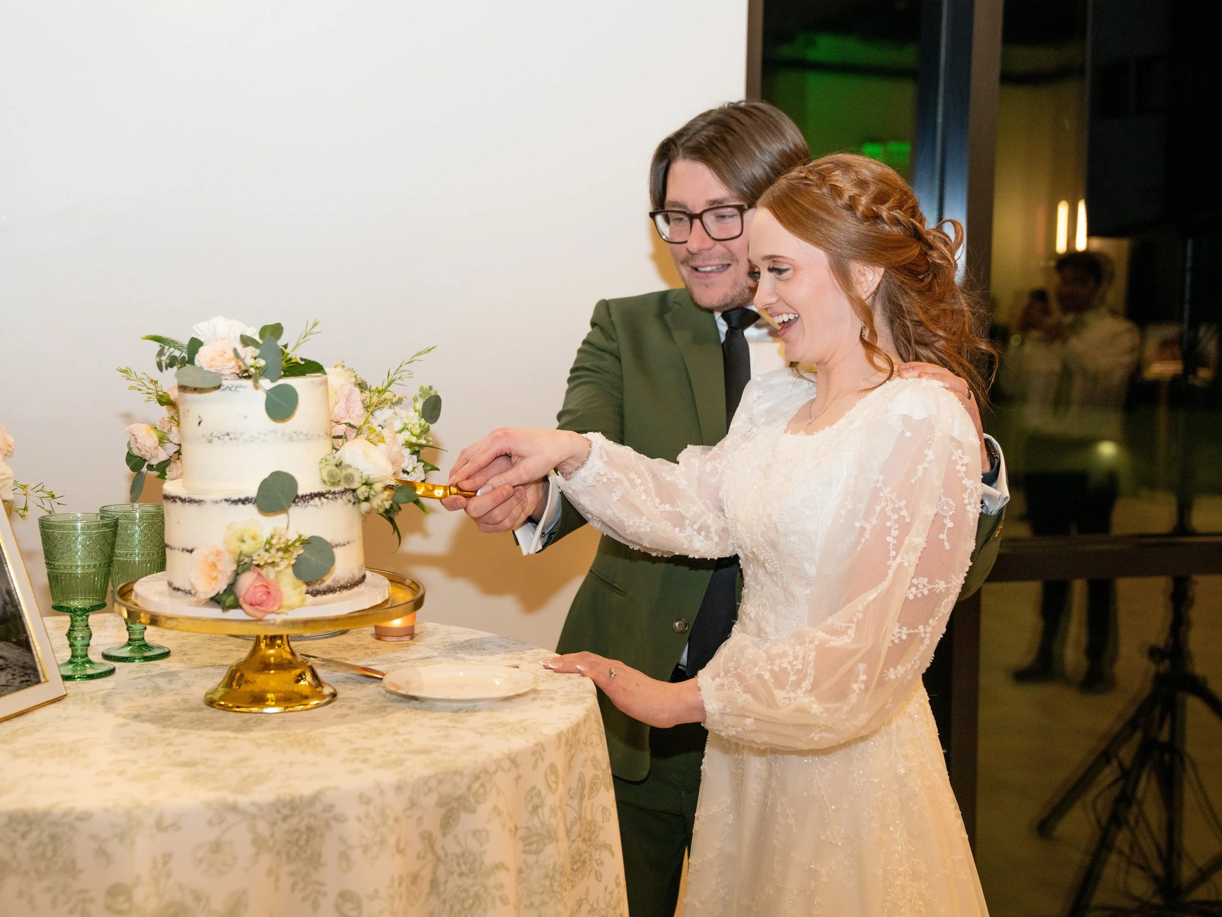 Bride and groom hold a cake knife together and cut into their white wedding cake.