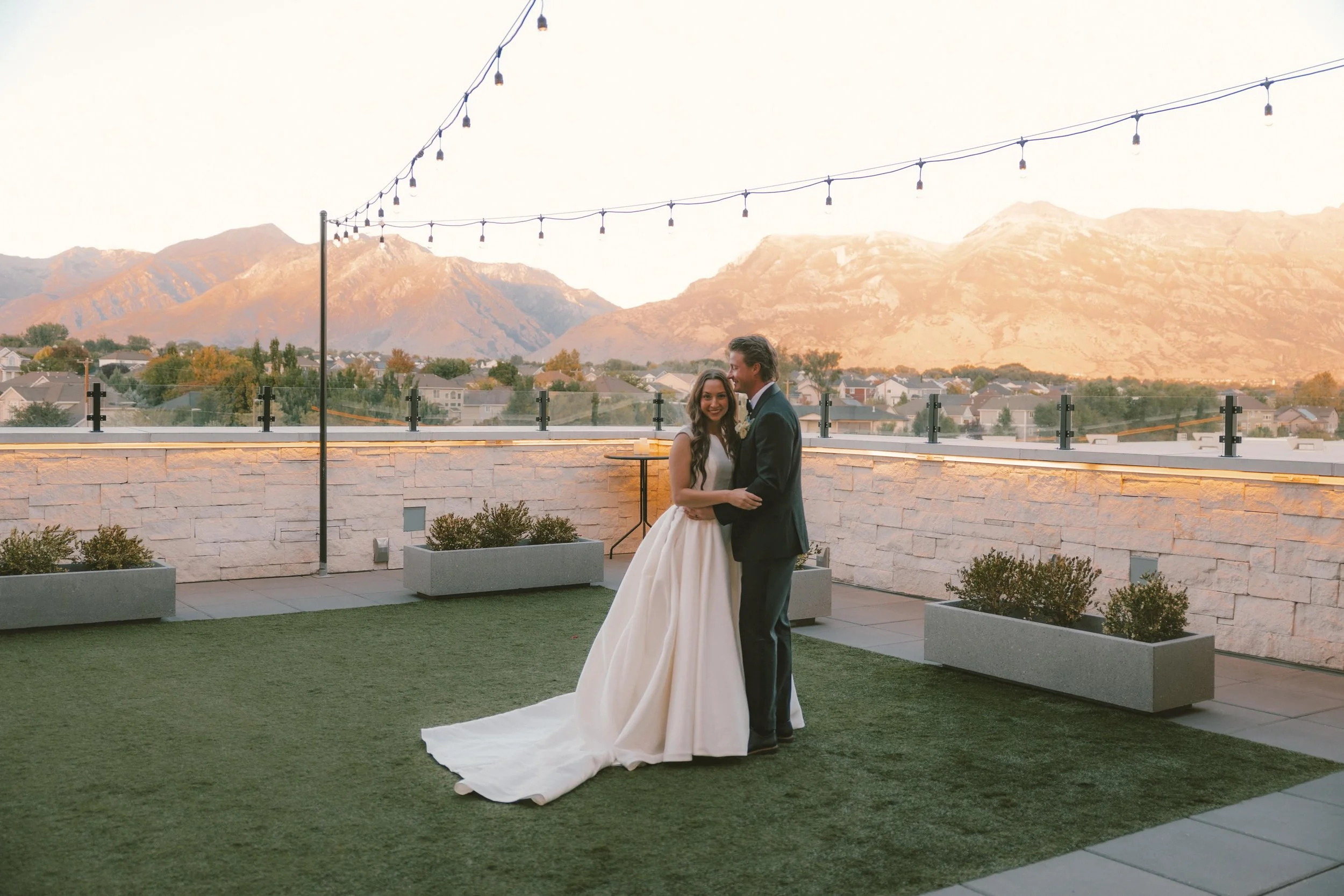 Bride and groom stand in the courtyard holding each other while the bride looks at the camera.