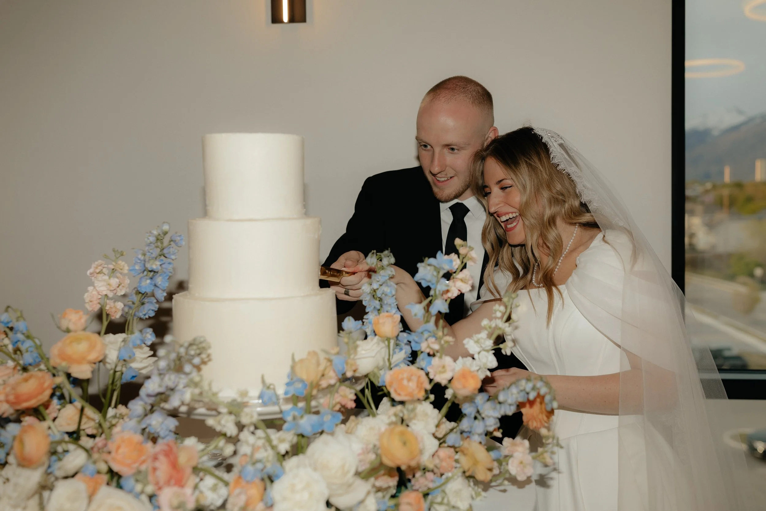 The bride and groom hold the knife together as they cut their white wedding cake.