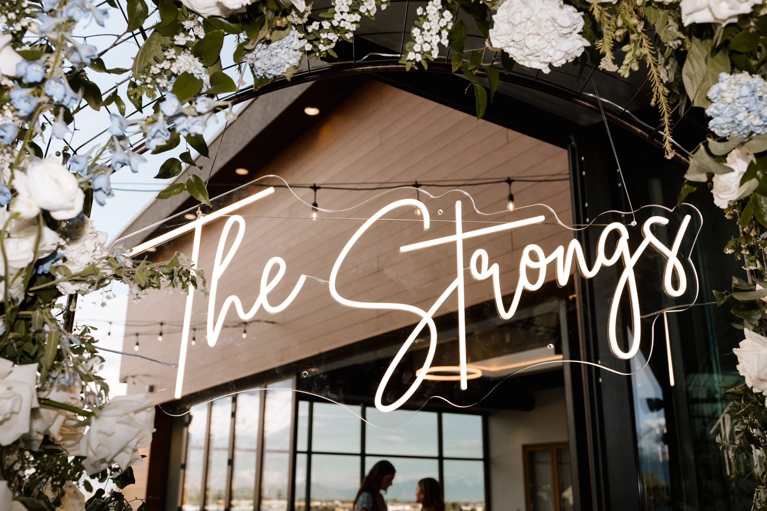 Neon wedding sign under an arch of flowers that says The Strongs.