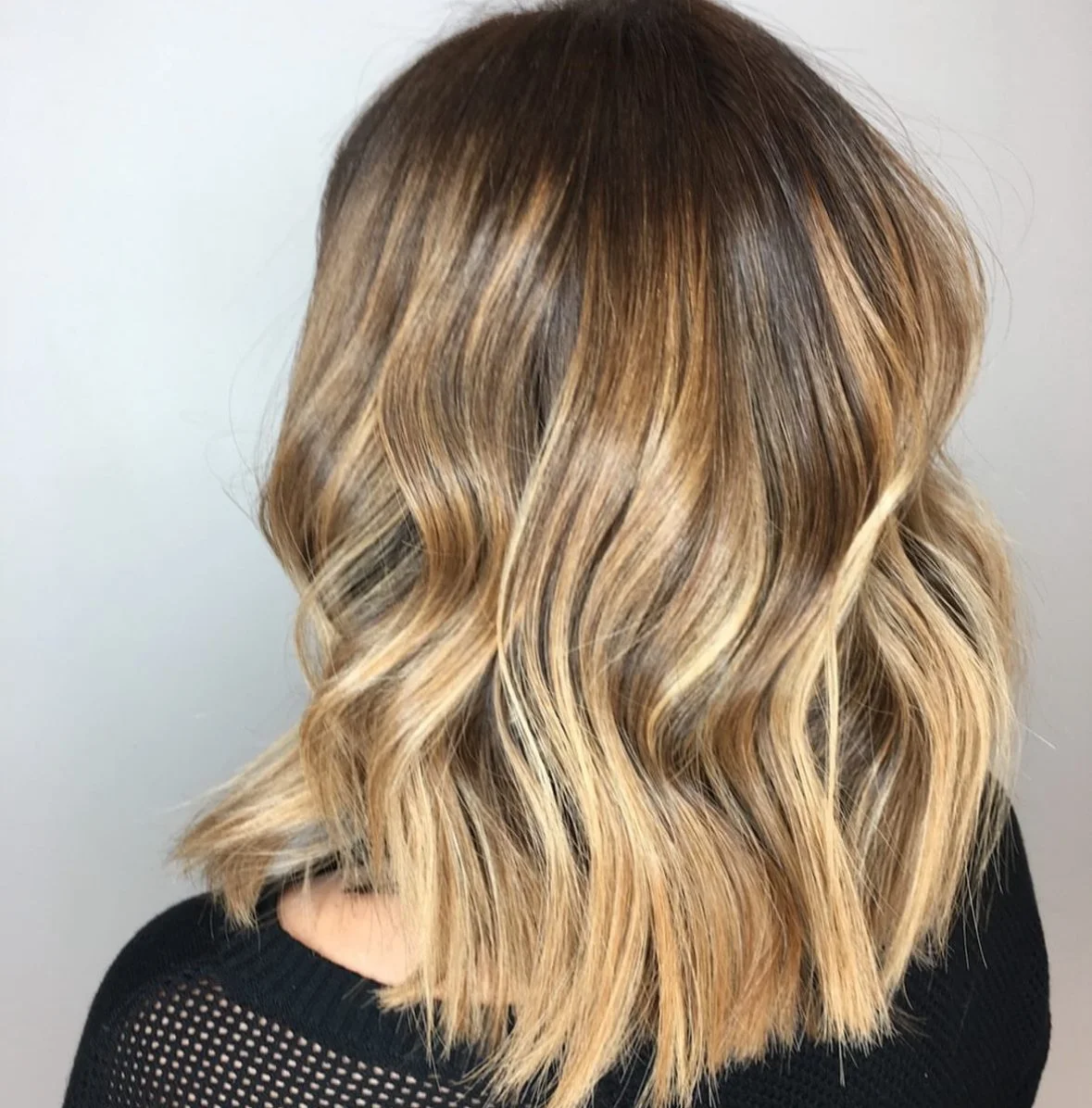 Shoulder-length wavy hair with dark roots and blonde highlights.