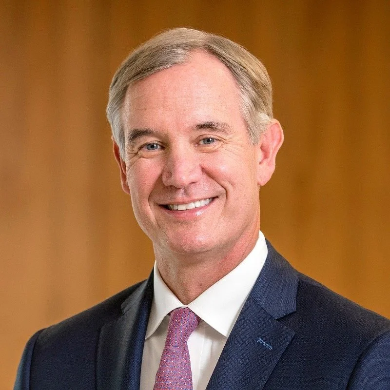 Man in a suit with a pink tie smiling, wooden background