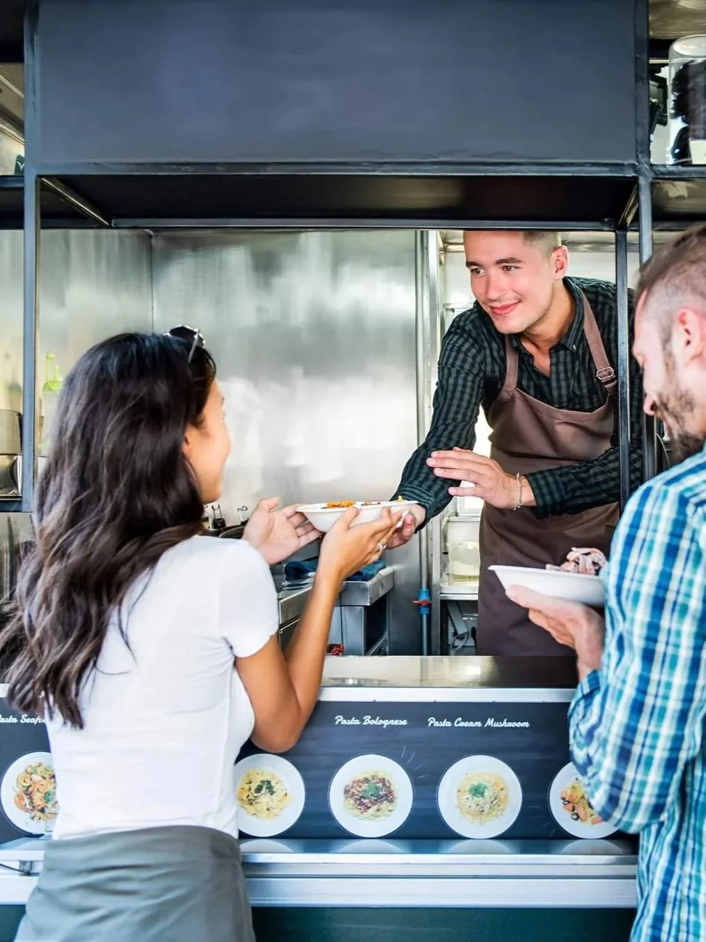 Food truck vendor handing a meal to customers at the service window.