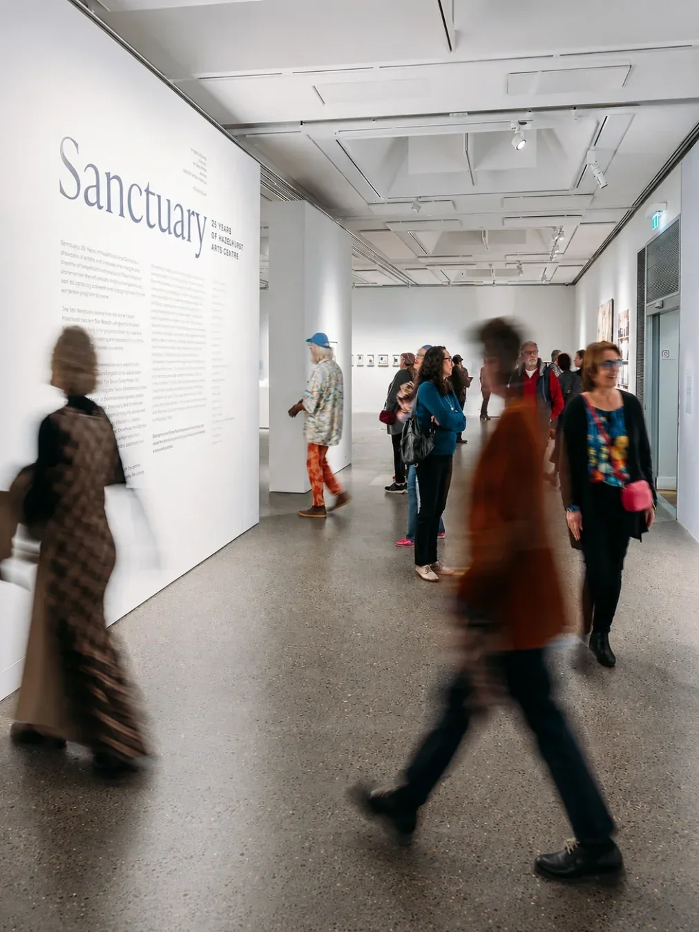 Visitors exploring a contemporary art exhibition inside Hazelhurst Arts Centre, with artworks displayed along bright white gallery walls.