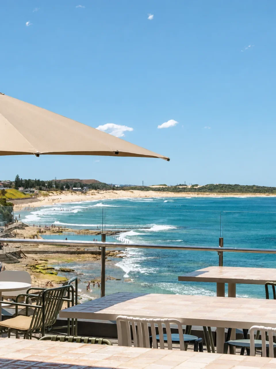 Beach and rock pool seen from the outdoor terrace at Cronulla RSL, with tables and a large umbrella.