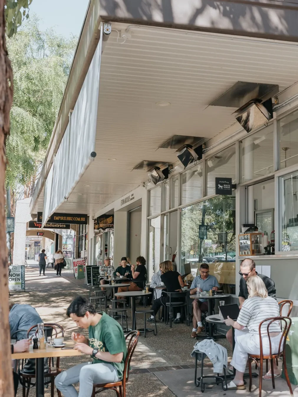 People eating and working at outdoor tables under a shopfront awning at Eliette in Sutherland.