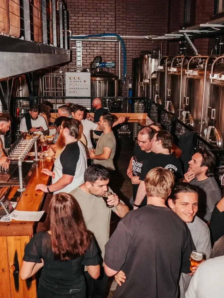 Crowd gathered inside Slim’s Brew in Engadine, enjoying drinks beside the brewery’s large stainless-steel tanks.